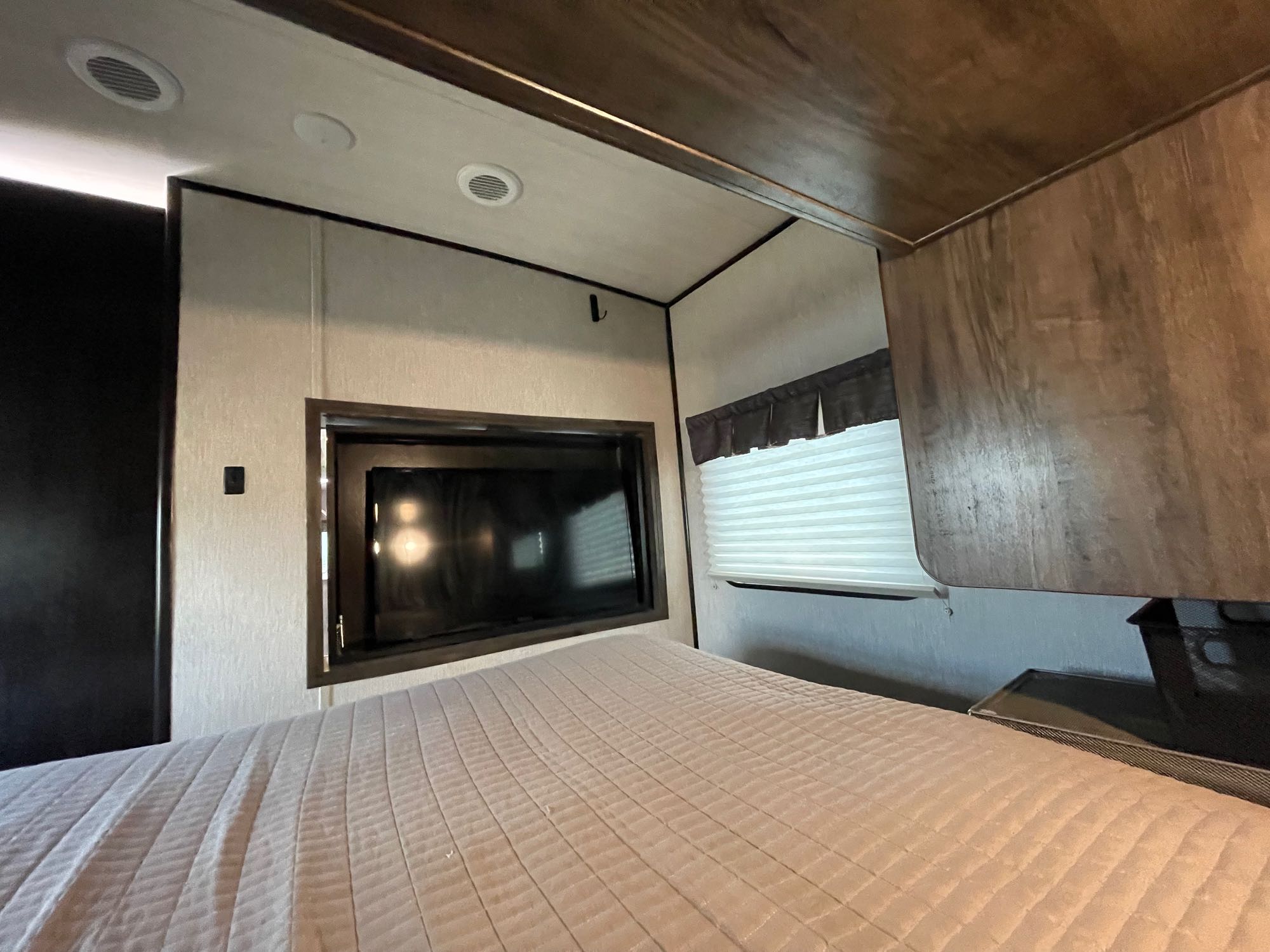 Cozy RV rental bedroom featuring a comfortable bed with a quilted cover, wall-mounted TV, and window with blinds.. Heartland RVs Mallard 2019