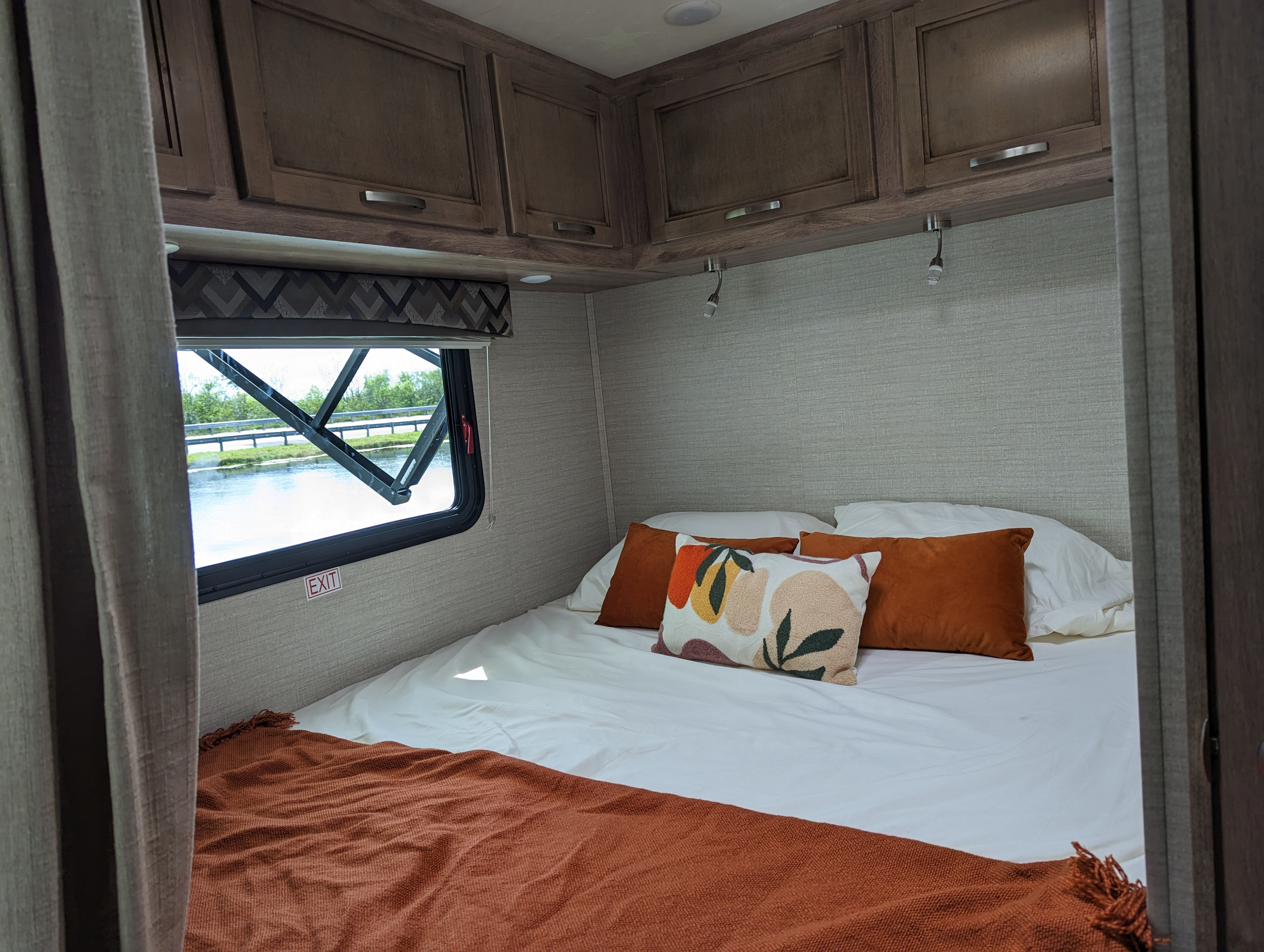 Comfortable RV rental bedroom featuring a bed with pillows, overhead cabinets, and a window with a water view.. Jayco Redhawk SE 2020