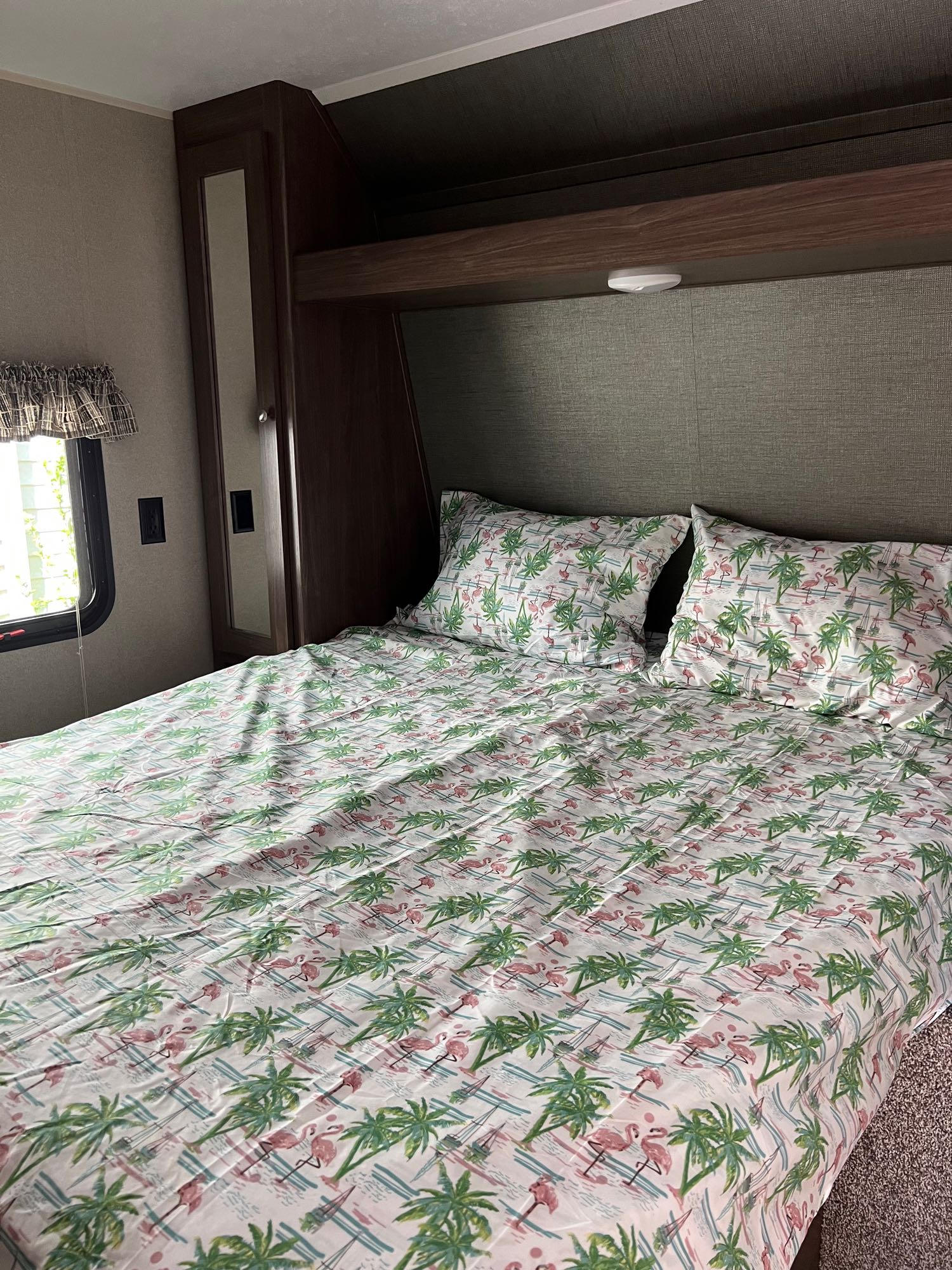 Cozy RV rental bedroom featuring a bed with fun flamingo and palm tree sheets, built-in cabinets, and a window.. Keystone RV Hideout 2018