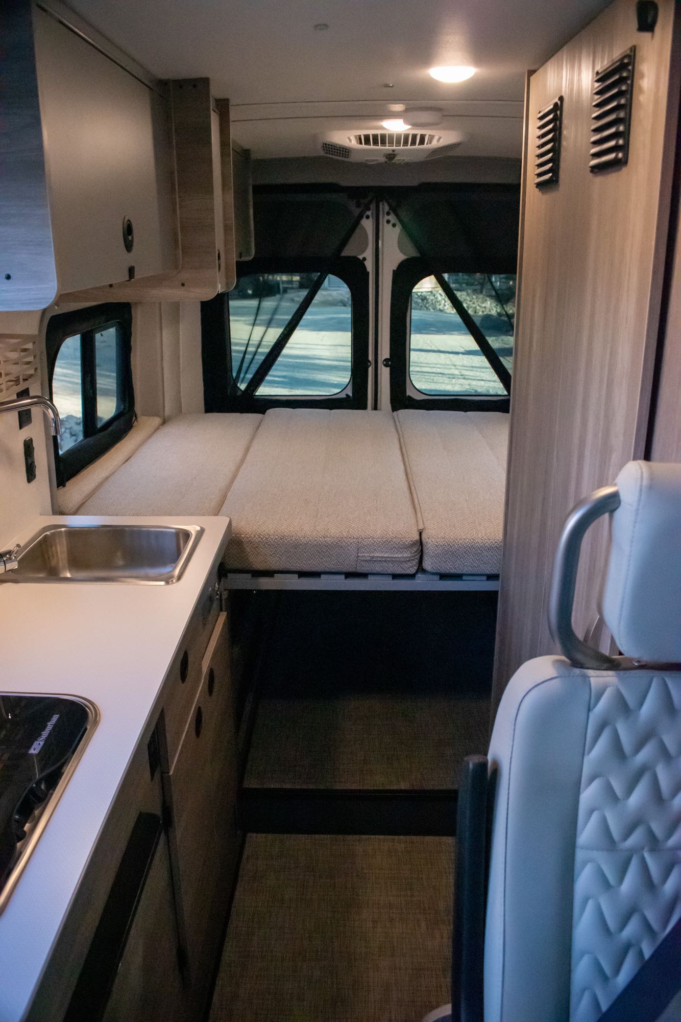 Cozy RV rental interior featuring a kitchen sink, overhead cabinets, and a comfortable bed setup in the rear. Ideal for road trips.. Winnebago Solis 59PX 2023