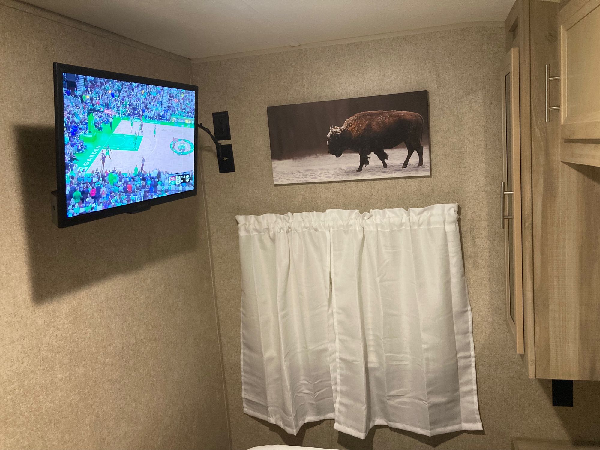 Inside a comfortable RV rental: Catch a basketball game on TV, admire bison art, and cozy curtains. Perfect for travel.. Coachmen 293QBCK 2020