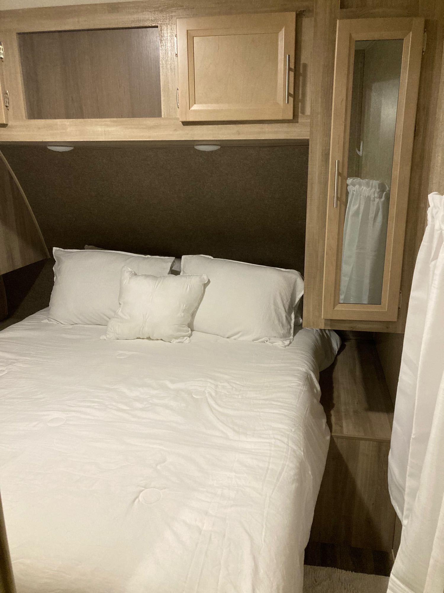 Cozy RV rental bedroom with white bed, pillows, and wooden cabinetry. Perfect for comfortable travel.. Coachmen 293QBCK 2020