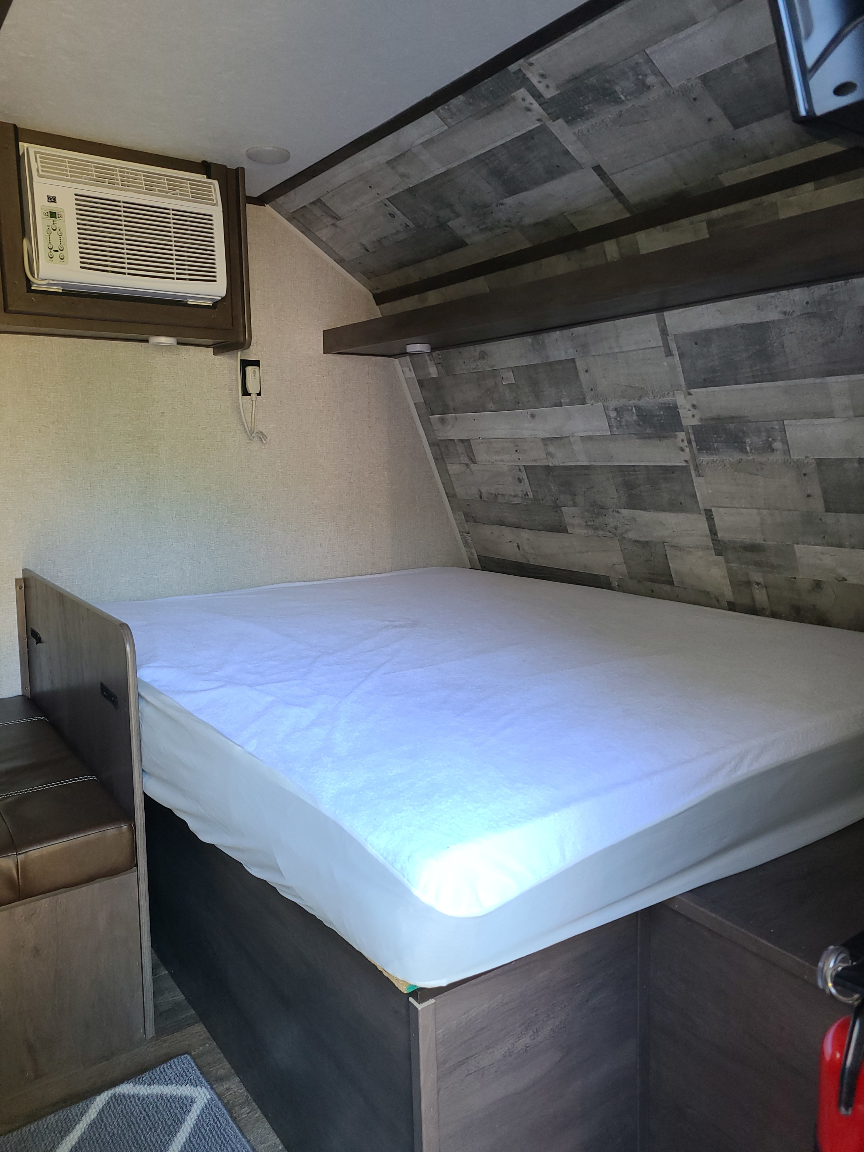 Inside an RV rental: a compact sleeping area with a bed, wall-mounted AC, and wood-paneled ceiling.. Dutchmen Coleman Lantern LT 2021