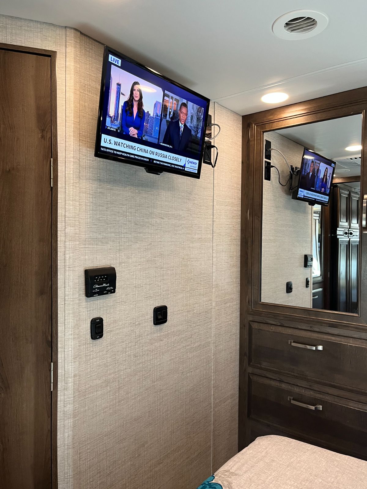 RV rental bedroom: Features a wall-mounted TV showing news, a thermostat, and storage. Enjoy comfort on your next adventure!. Entegra Coach Esteem 2021