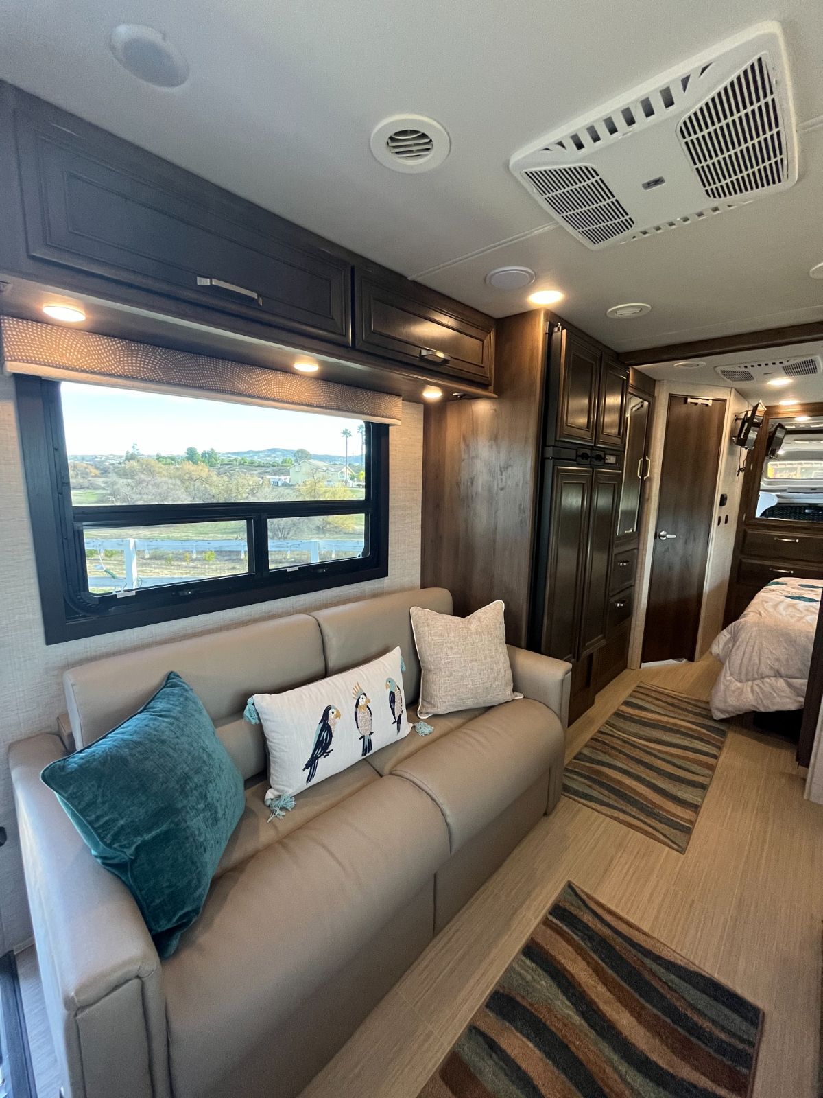 Cozy RV rental interior: sofa, window, well-lit overhead cabinets, fridge, and private bedroom.. Entegra Coach Esteem 2021