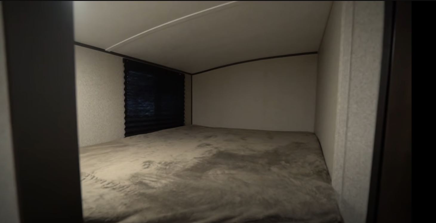 Cozy RV rental sleeping area featuring a bed with a gray blanket, a dark window blind, and light-colored walls.. Keystone RV Springdale 2019