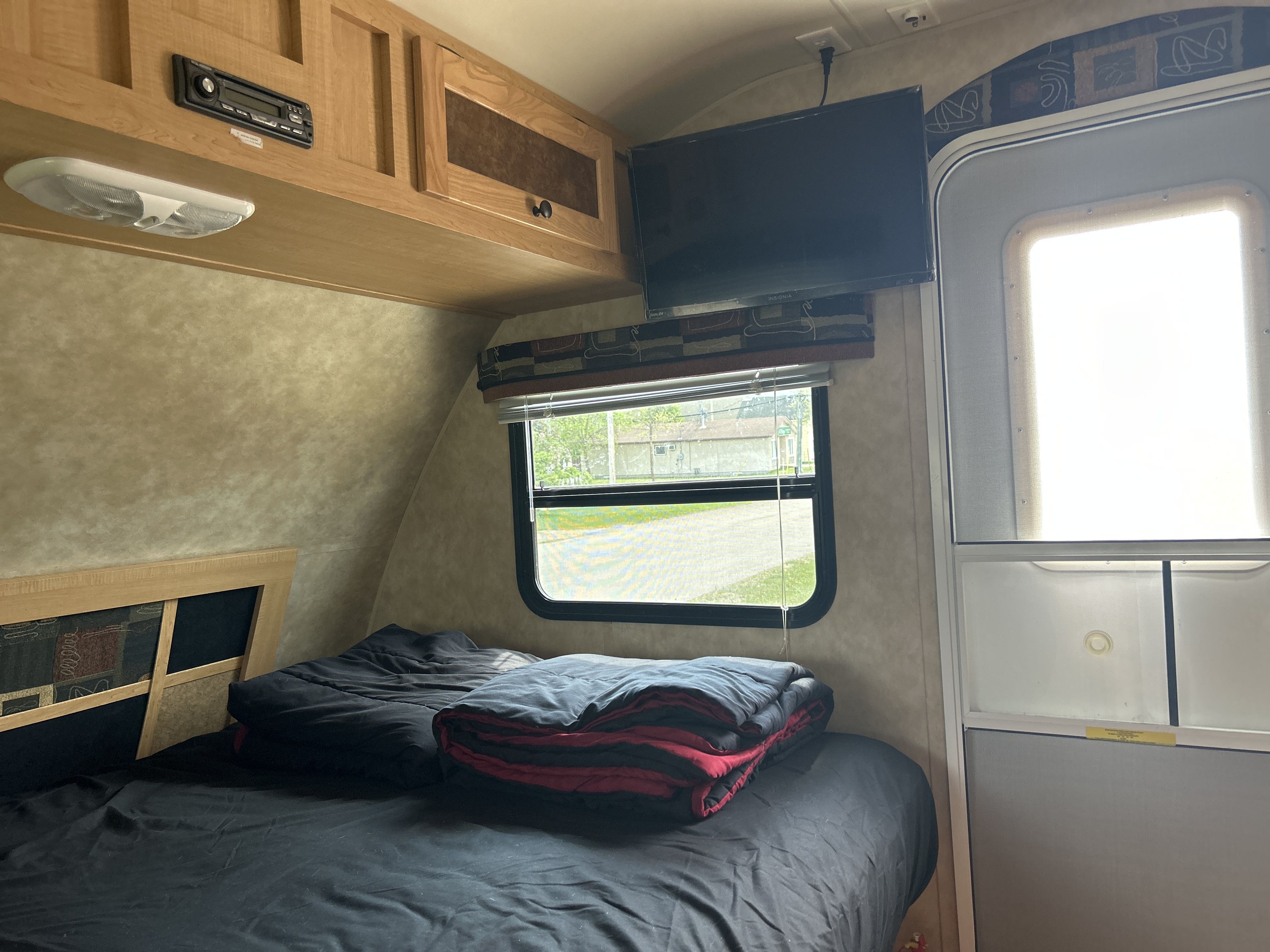 RV rental bedroom: comfy bed, overhead storage, TV, and window view, adjacent to the entrance door.. Ez Coyote lite 2010