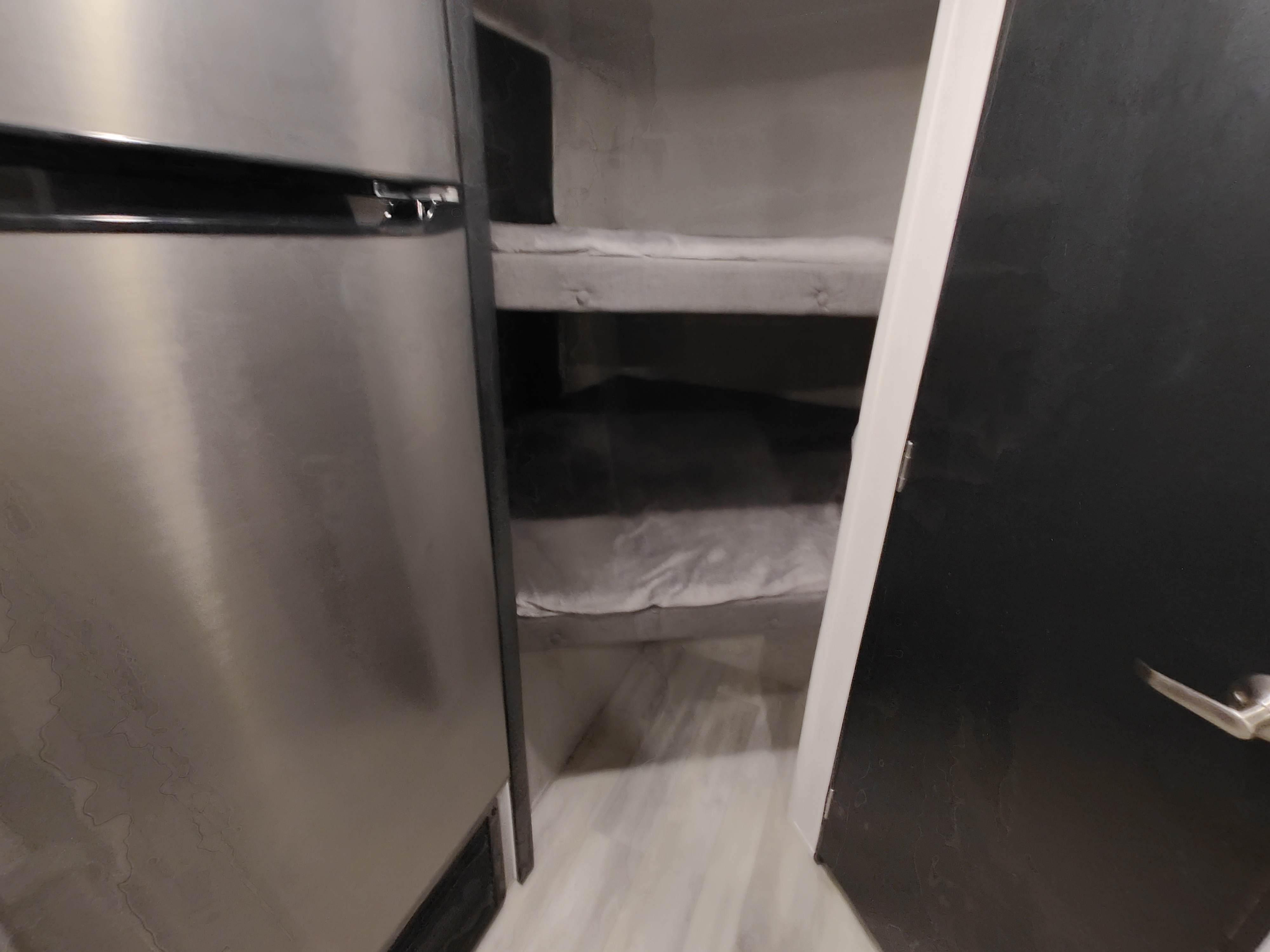 RV rental interior features: a stainless steel refrigerator and two built-in bunk beds with white linens, maximizing compact space.. Forest River Tracer 2022