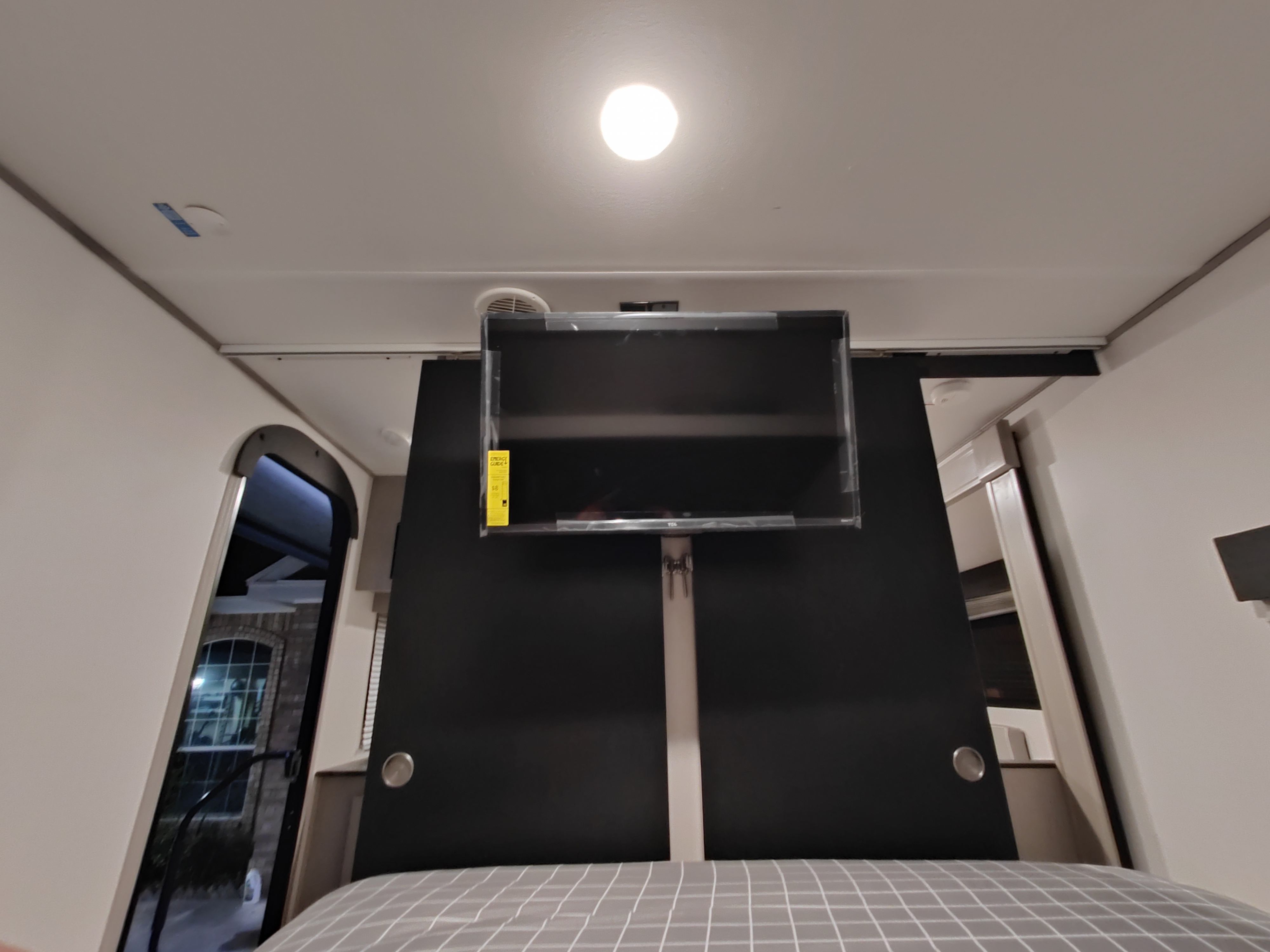 Cozy RV rental bedroom featuring a wall-mounted TV above a checkered bed, with a large window view.. Forest River Tracer 2022