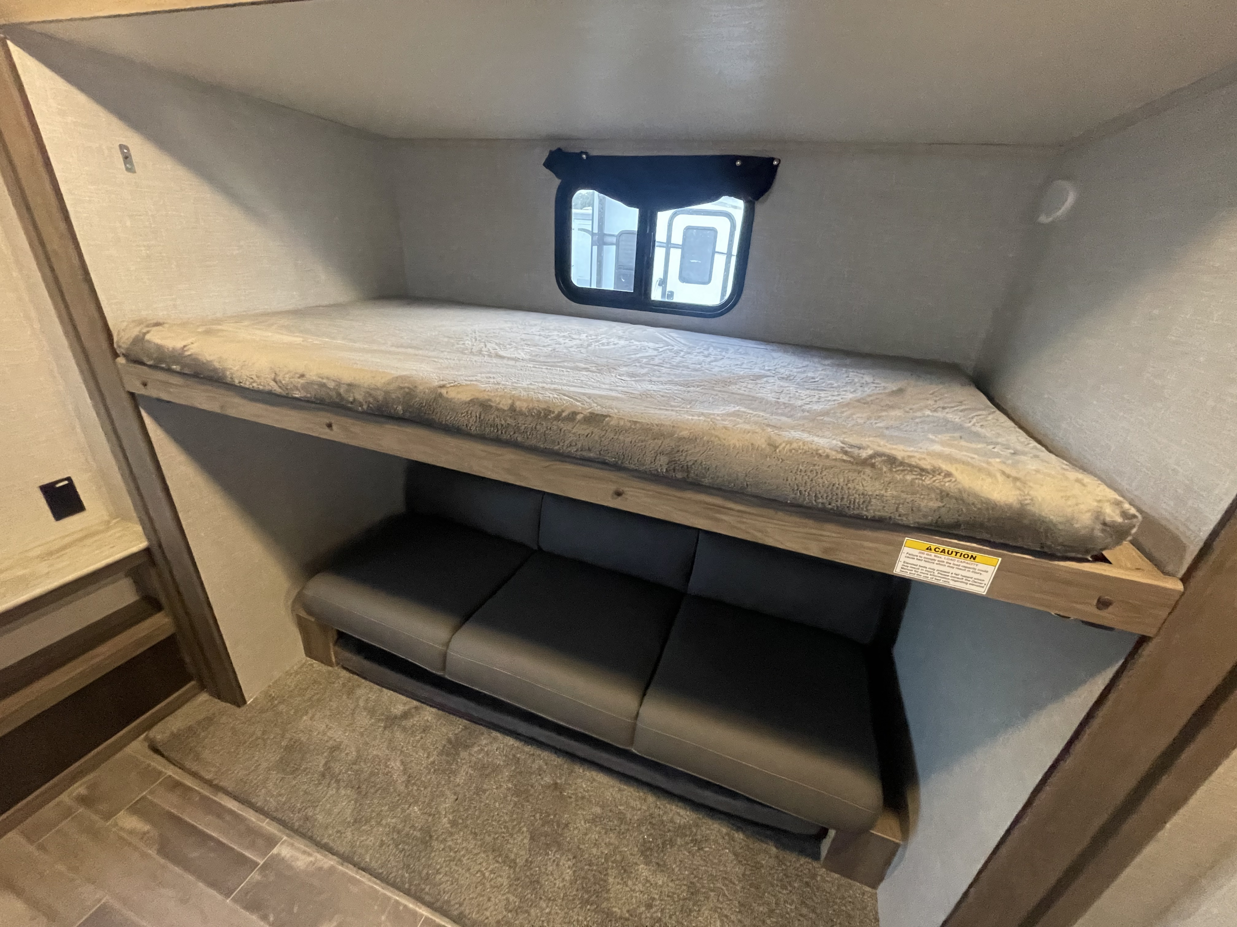 This RV rental features a cozy bunk bed above a convertible sofa seating area, ideal for compact family travel.. Crossroads RV Zinger 2023