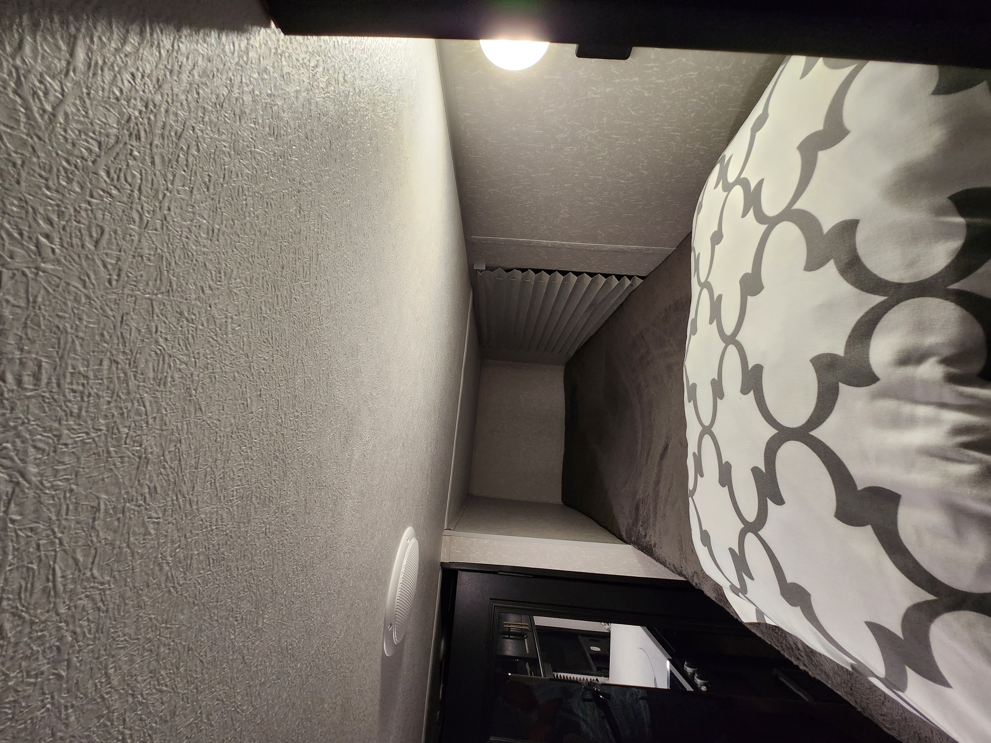 Inside an RV rental: View from a bed with patterned bedding, looking down a textured wall hallway with a vent and a door ahead.. Forest River Cherokee Wolf Pup 2022