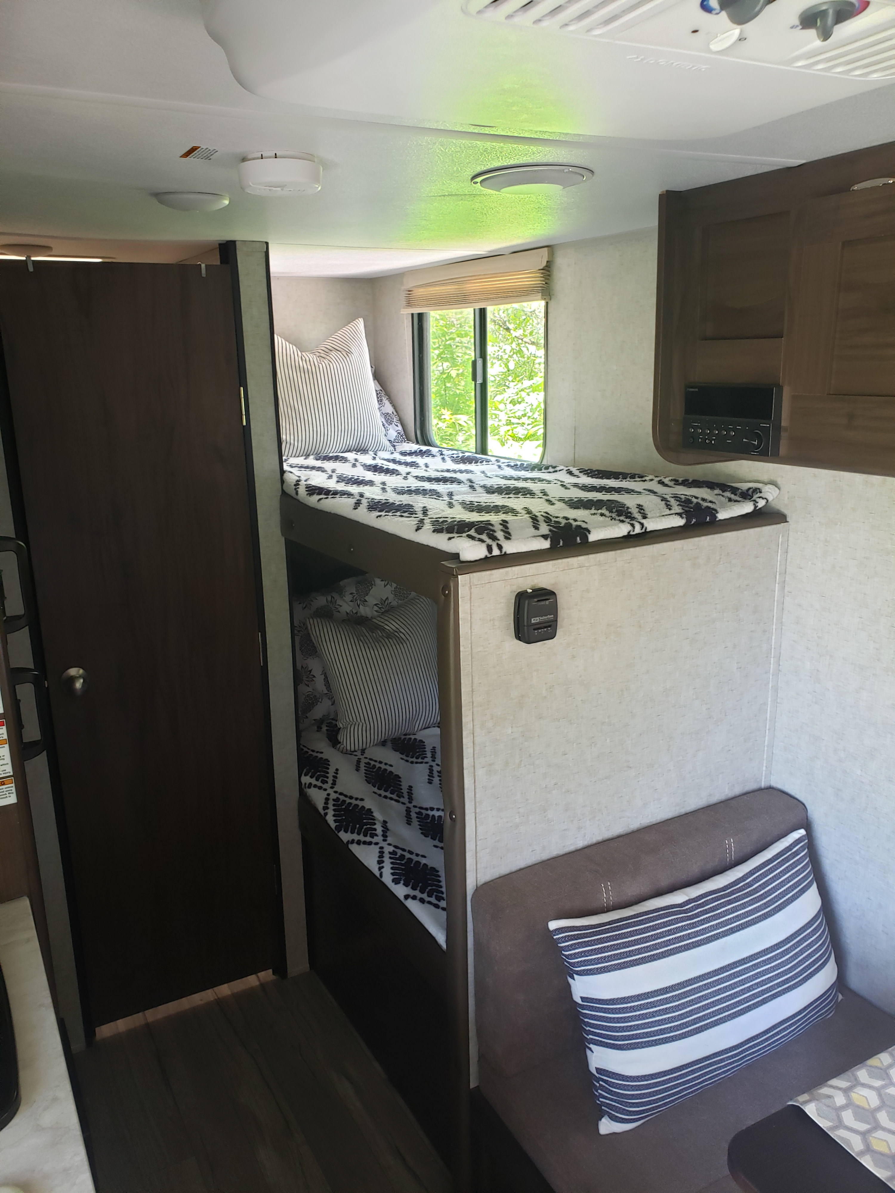 Cozy RV rental interior with bunk beds, striped pillows, a window, and a door to a private room/bathroom.. Forest River Cherokee Wolf Pup 2019