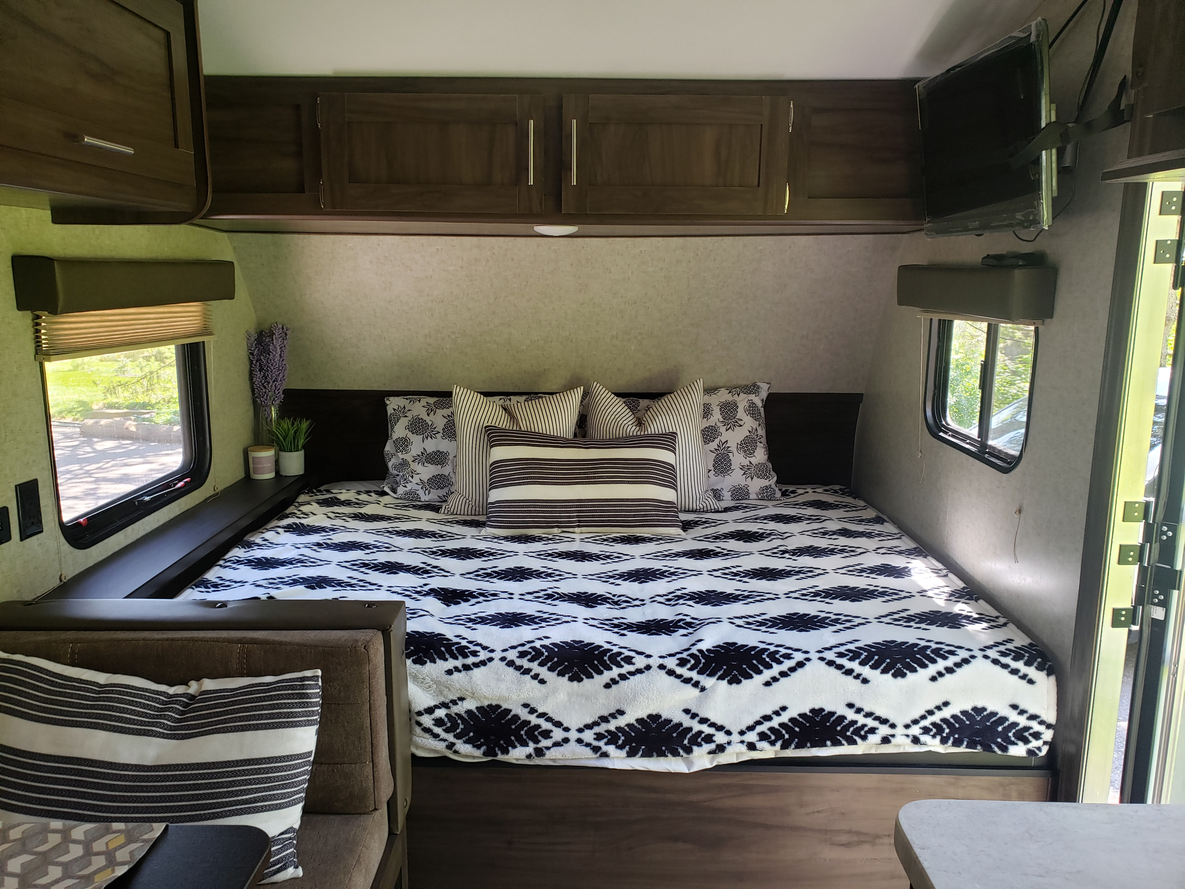 Inside a spacious RV rental bedroom: large bed with black and white bedding, overhead cabinets, TV, and windows.. Forest River Cherokee Wolf Pup 2019
