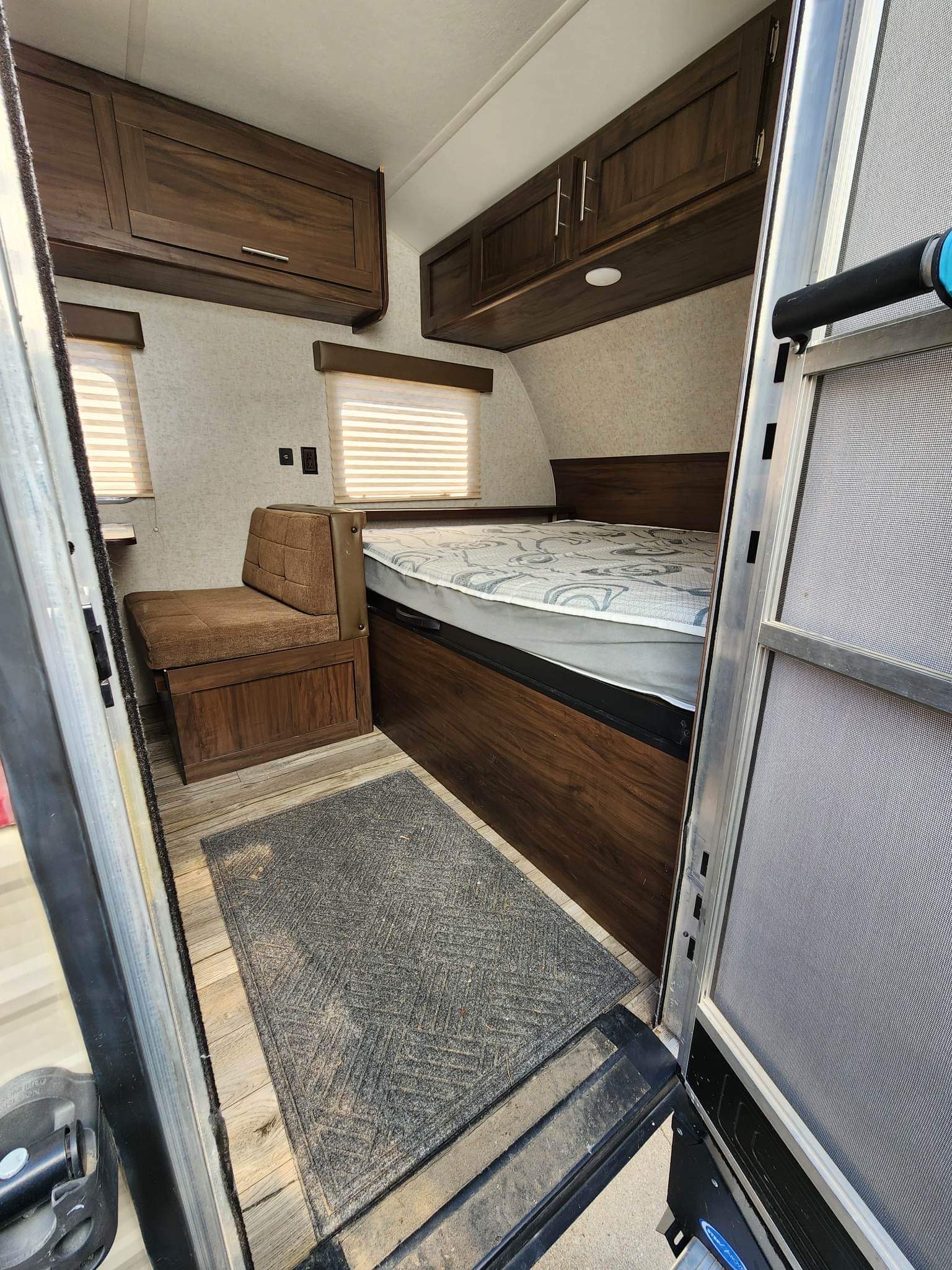 Interior view of an RV rental showing a neatly made bed, dinette seat, and ample overhead cabinets for storage.. Forest River Cherokee Wolf Pup 2018
