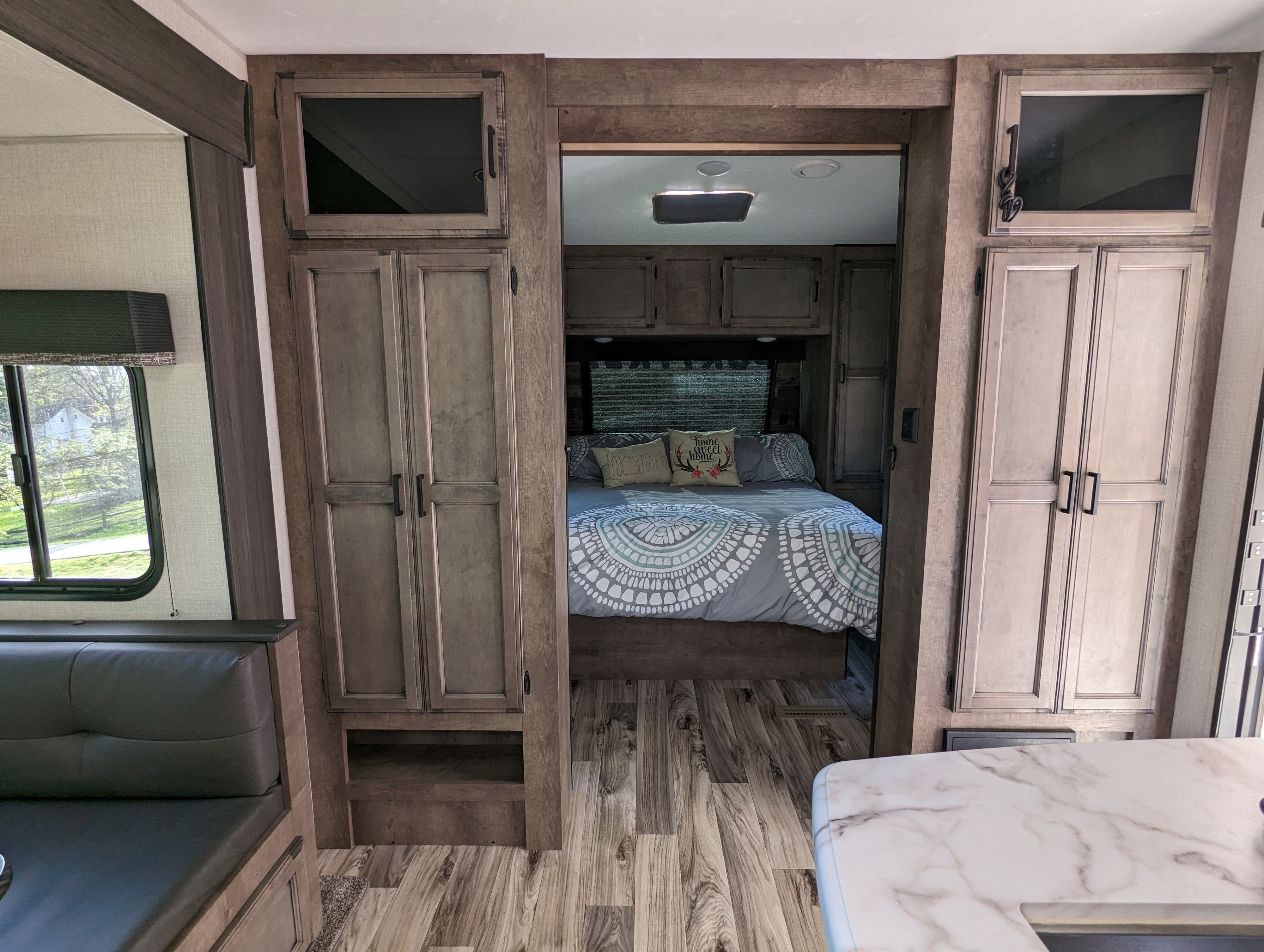 View inside an RV rental, highlighting the bedroom with decorative bedding and the adjacent living area's wood-look interior.. Sport Trek Sport Trek Trailer 2021