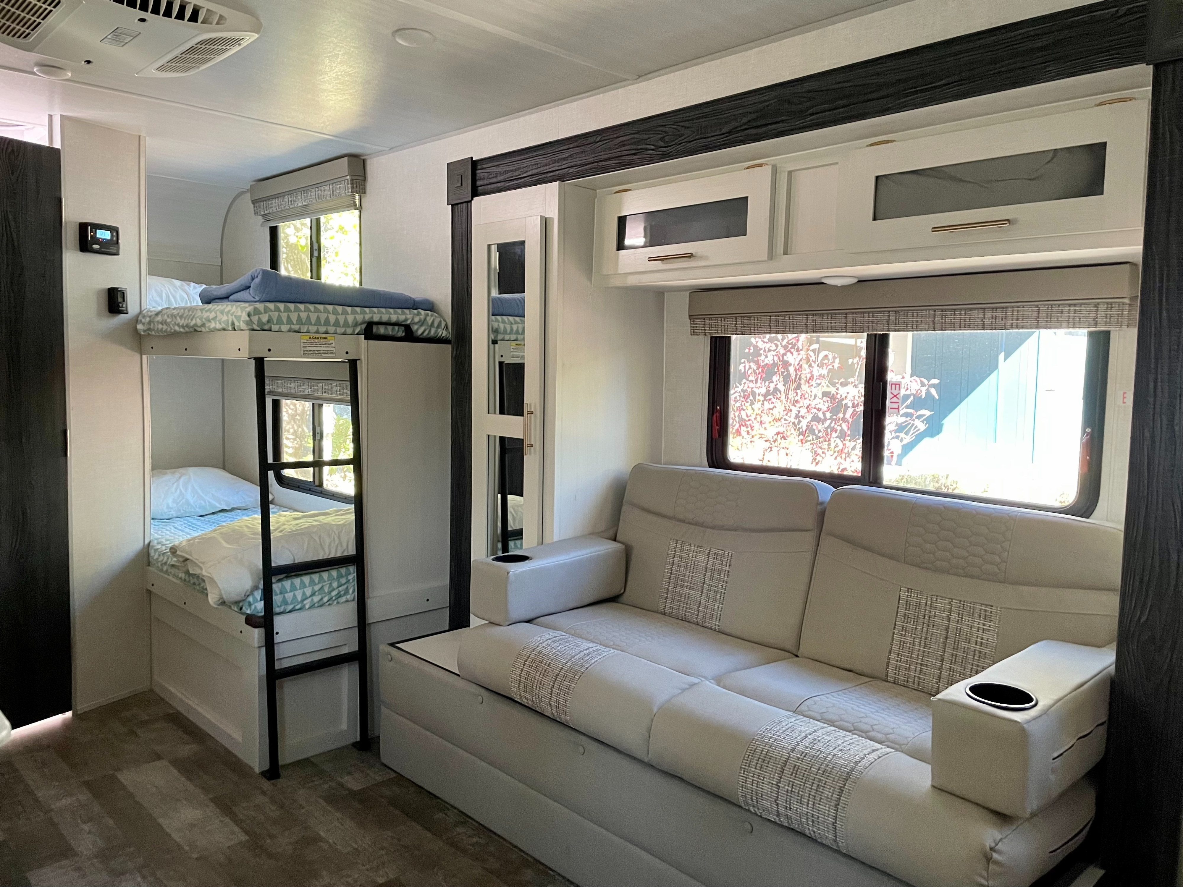 Bright RV rental interior showing bunk beds, a light-colored sofa with built-in cup holders, and overhead cabinets.. R-Pod Hood River Edition 2021