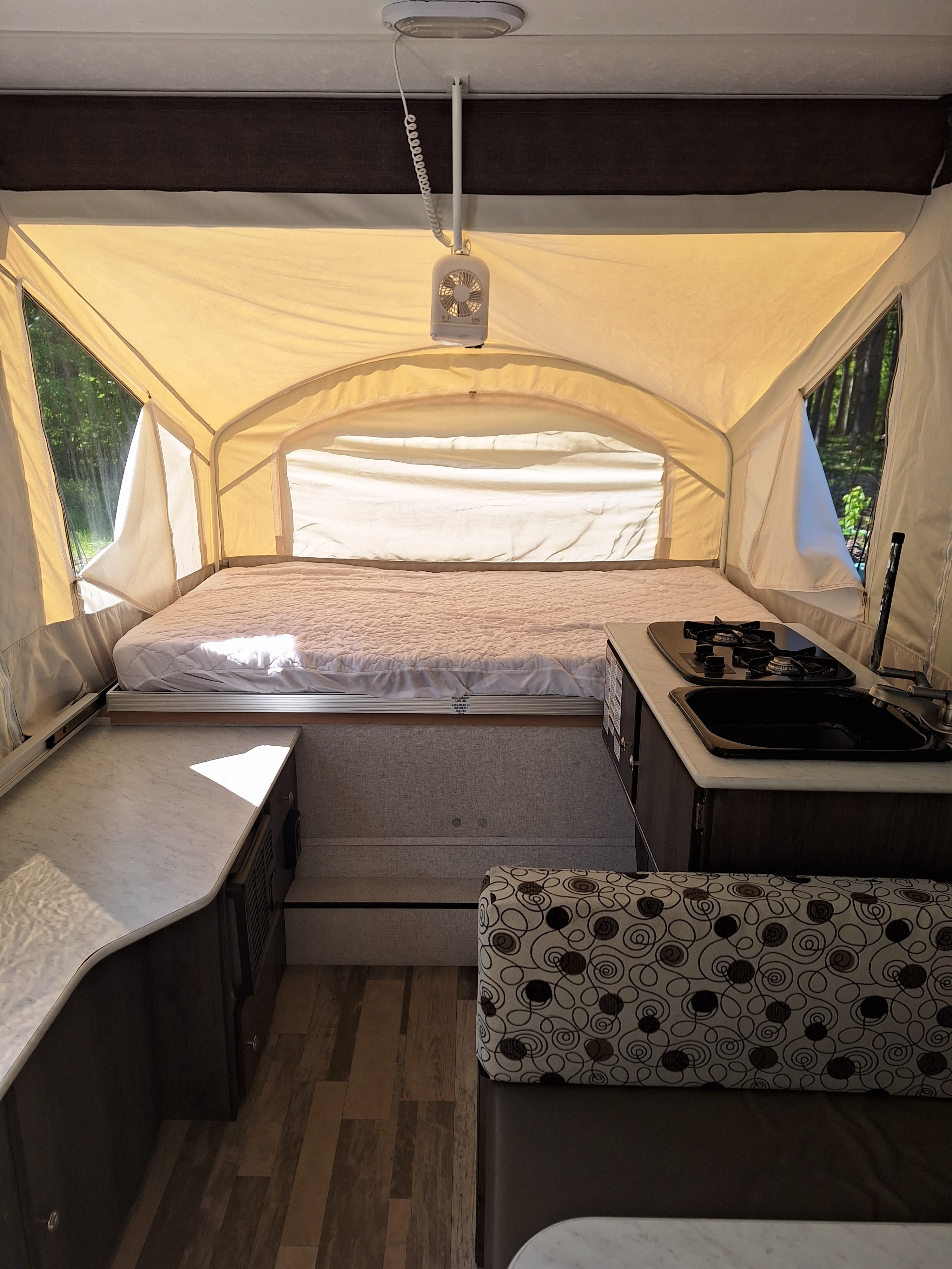 Interior of an RV rental: a pop-up bed, compact kitchen with sink and stove, and cozy seating.. Grand River Other 2019