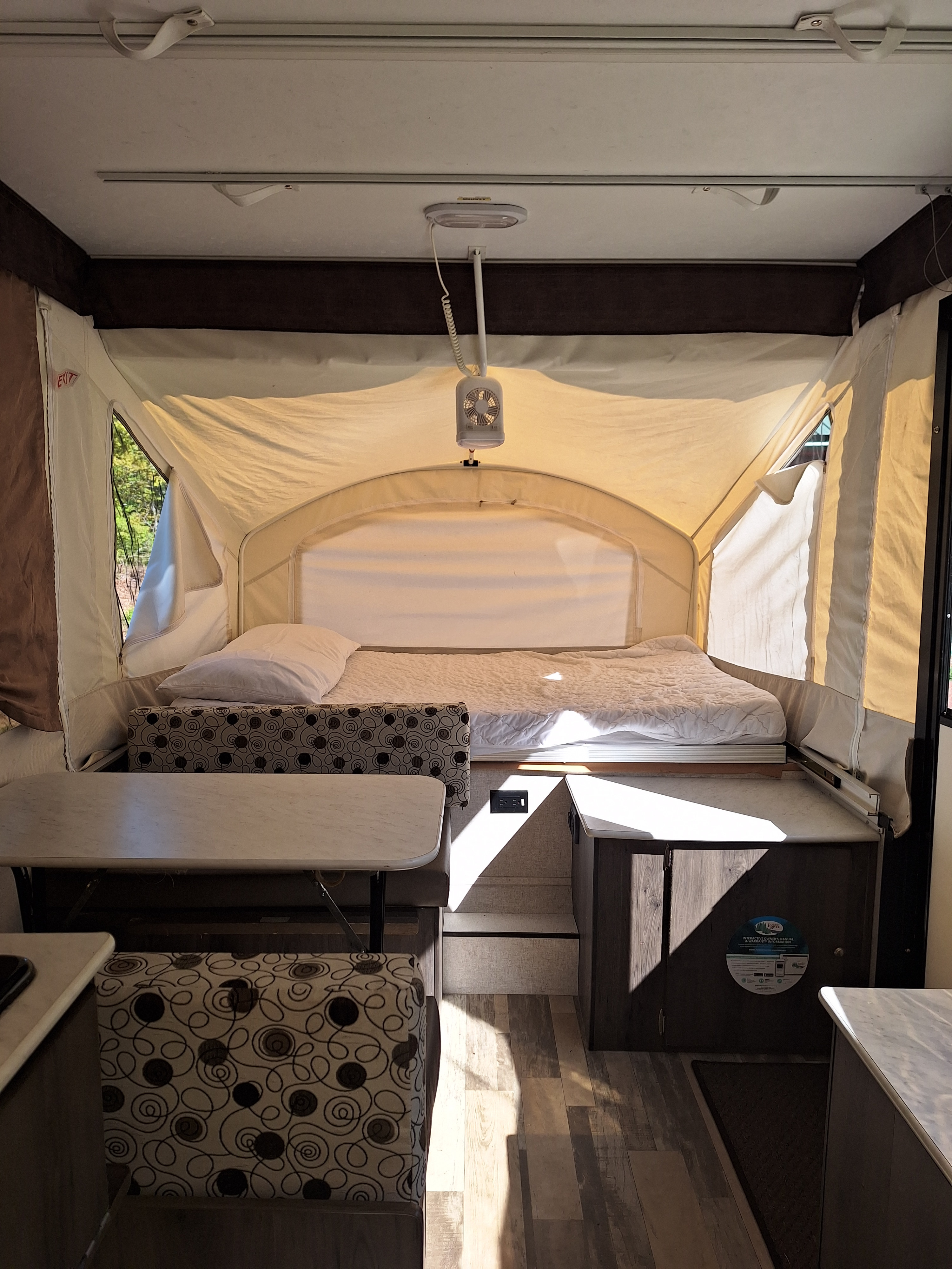 RV rental interior: A bright pop-up camper with a large bed, dining area with patterned cushions, and wood-look flooring.. Grand River Other 2019