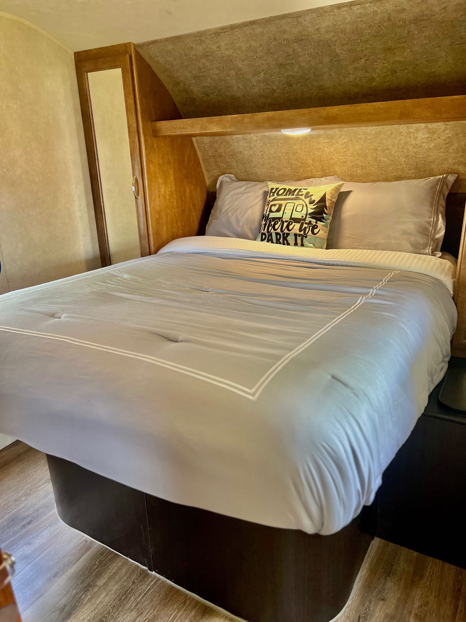 Cozy RV rental bedroom featuring a large bed with gray bedding, built-in storage, and wood-look flooring.. Forest River Salem 2016