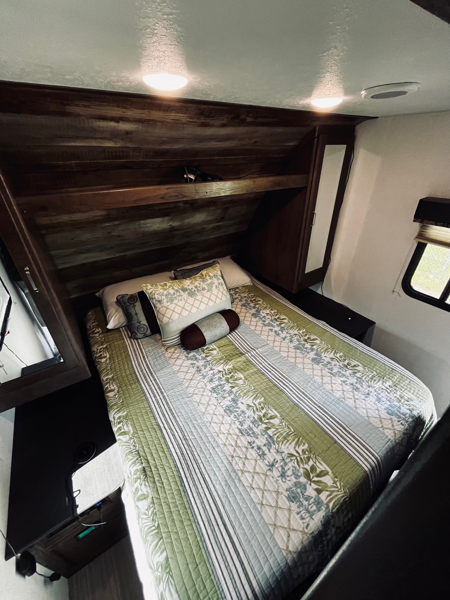 Cozy RV rental bedroom featuring a bed with patterned quilt, overhead lights, and a window. Ideal for travels.. Keystone RV Passport Ultra Lite 2019