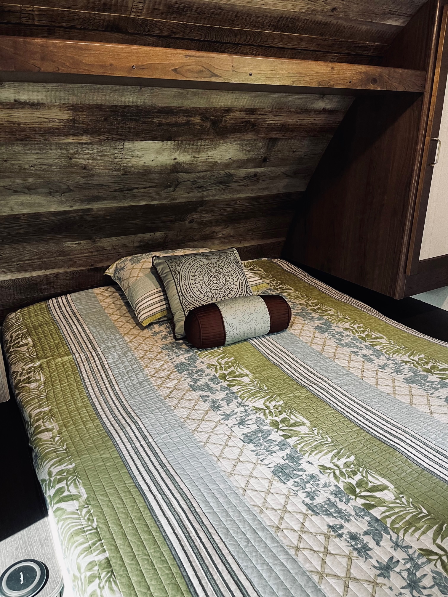 Comfortable RV rental bed with a green and white quilt, rustic wood paneling, and an adjacent cabinet.. Keystone RV Passport Ultra Lite 2019