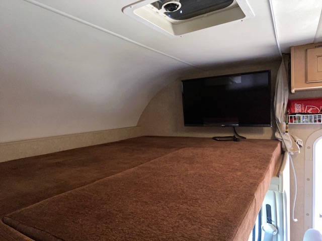 RV rental cab-over bunk featuring a comfy bed and mounted TV. Ideal RV interior for relaxation and sleeping.. Thor Chateau 2015