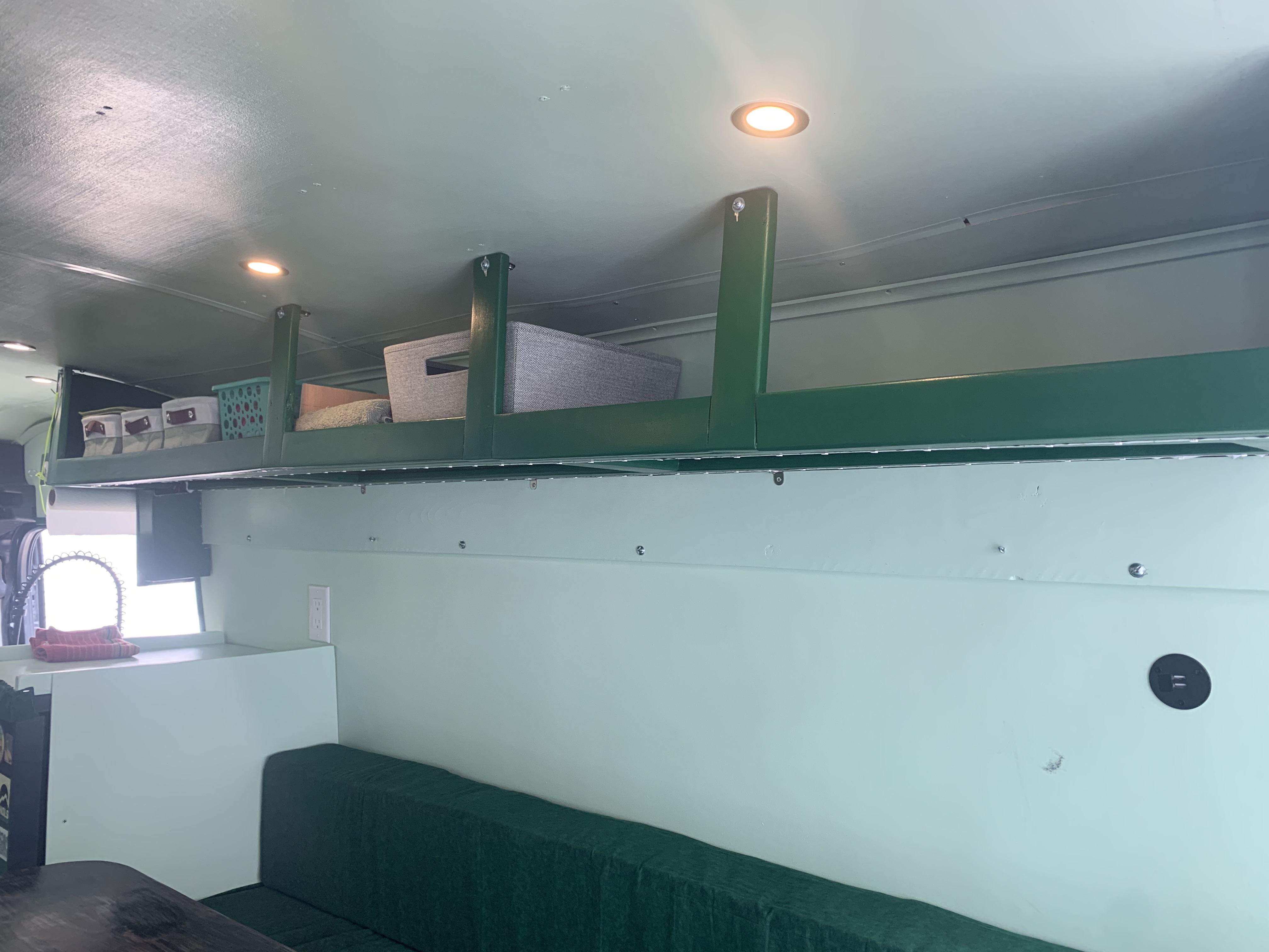 RV rental interior with light green walls, green overhead storage, bright lighting, and a dark green sofa.. Ford Transit 2022