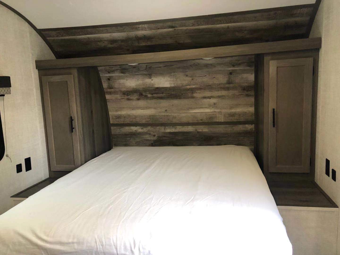 This RV rental bedroom features a cozy bed with white sheets, stylish wood paneling, and built-in storage cabinets. Perfect for travel comfort.. Grand River 25BH 2023