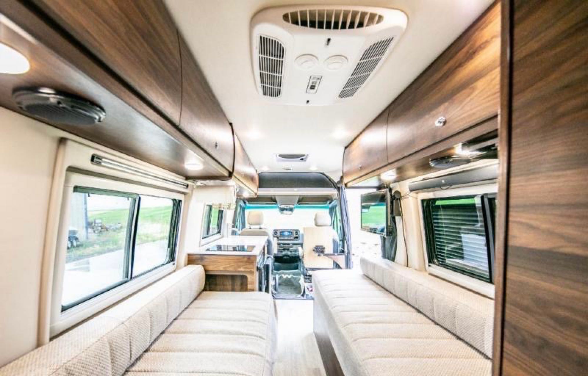 Spacious, modern RV rental interior with dual benches, overhead storage, and a view to the driver's cabin, perfect for travel.. Winnebago Boldt 2020