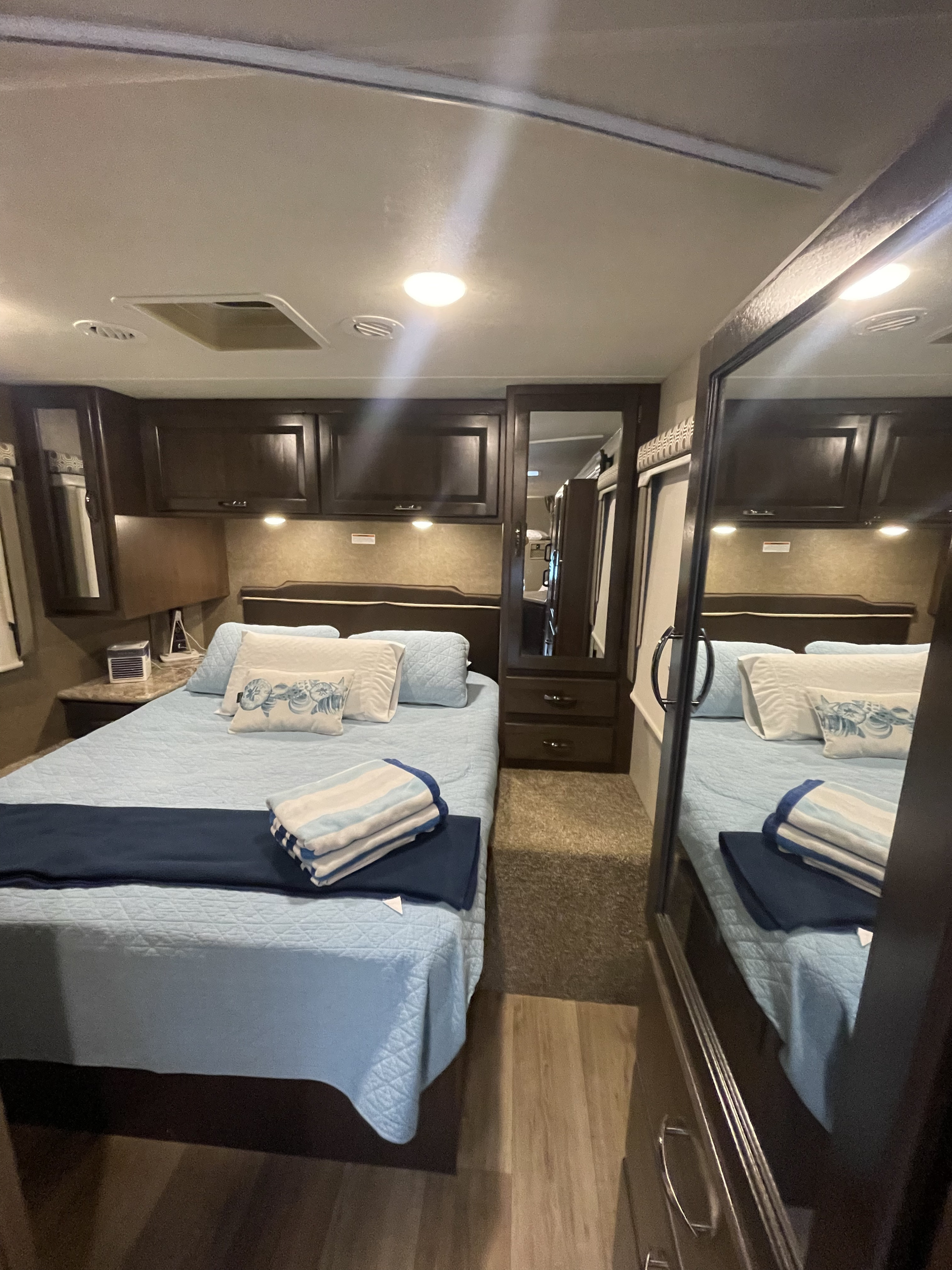 Cozy RV rental bedroom with a comfy bed, overhead cabinets, and a mirrored closet, offering comfortable travel.. Thor Four Winds 2020
