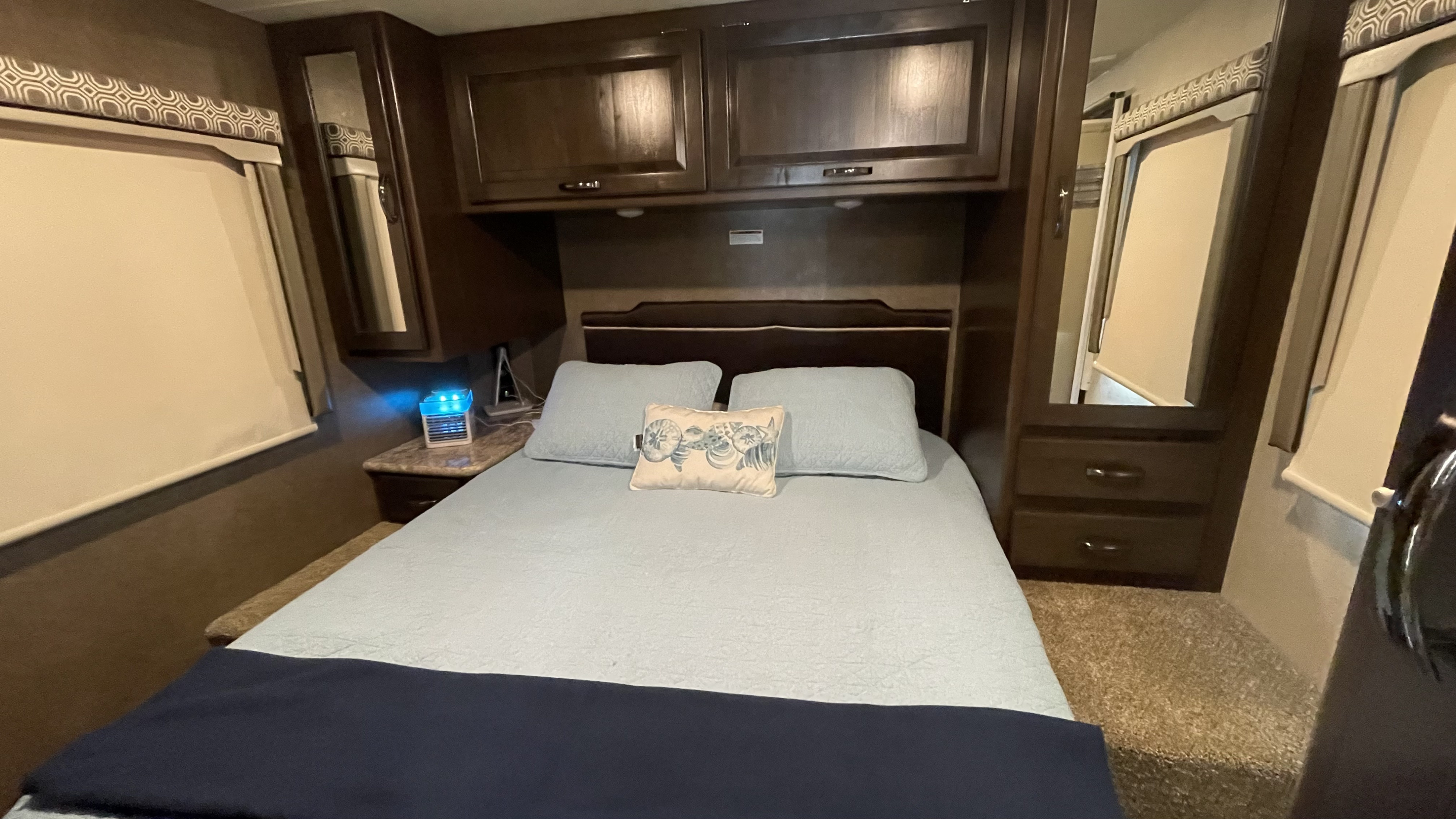 This RV rental shows a neatly made bedroom with light blue bedding, overhead cabinets, and mirrored wardrobe for your travels.. Thor Four Winds 2020