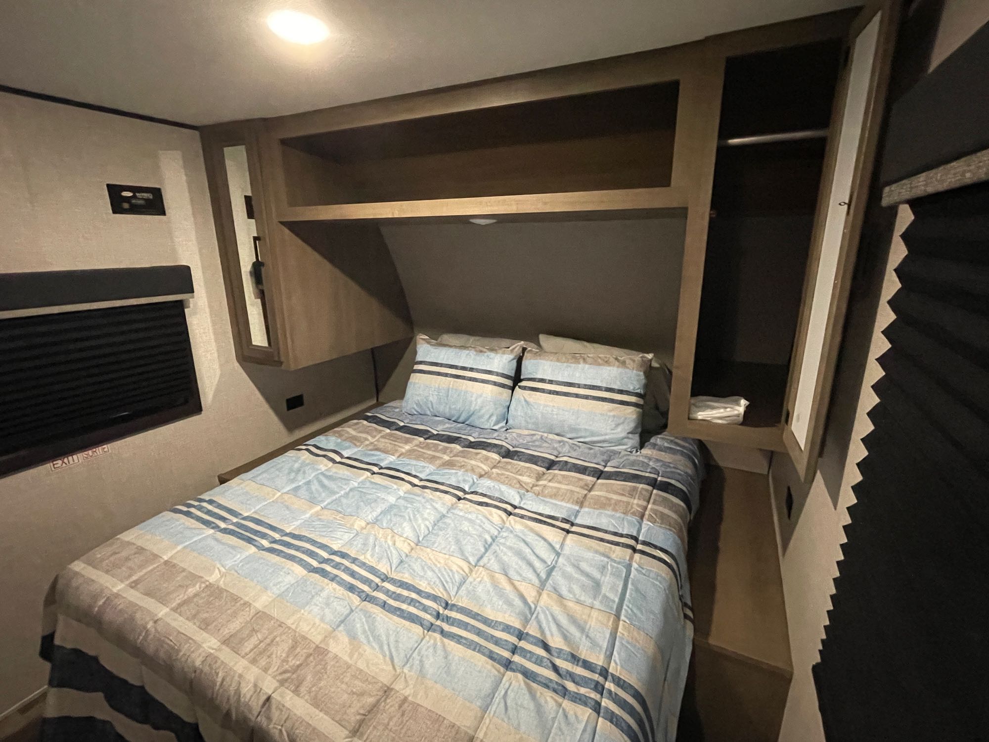 Cozy RV rental bedroom featuring a striped bed, overhead storage, and window blind. Ideal for compact travel.. Highland Ridge RV Open Range 2023