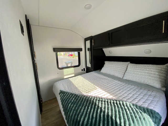 Modern RV rental bedroom with a compact bed, sleek black cabinets, and natural light from the window.. Forest River Cherokee Grey Wolf 2022