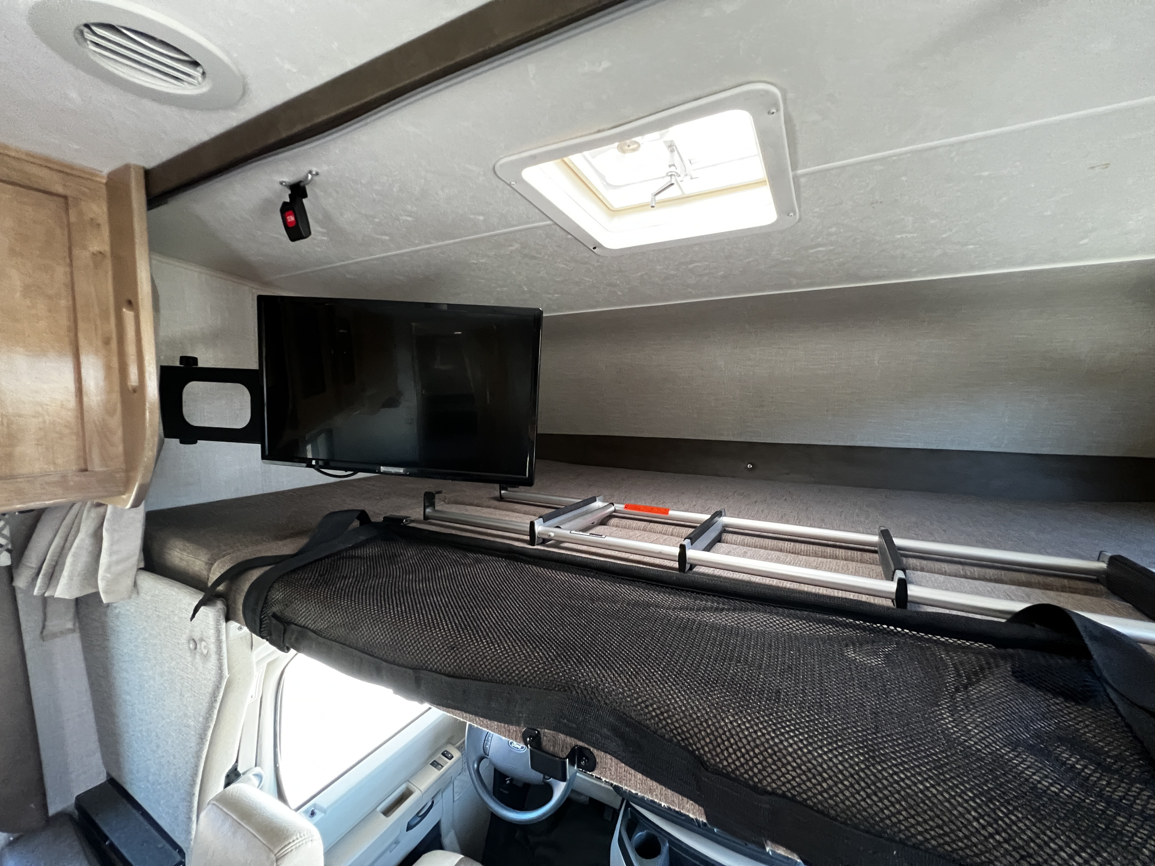 Spacious RV rental cabover bunk featuring a mounted TV, ladder, and mesh safety net for comfortable travels.. Forest River Coachmen Leprechaun 2020