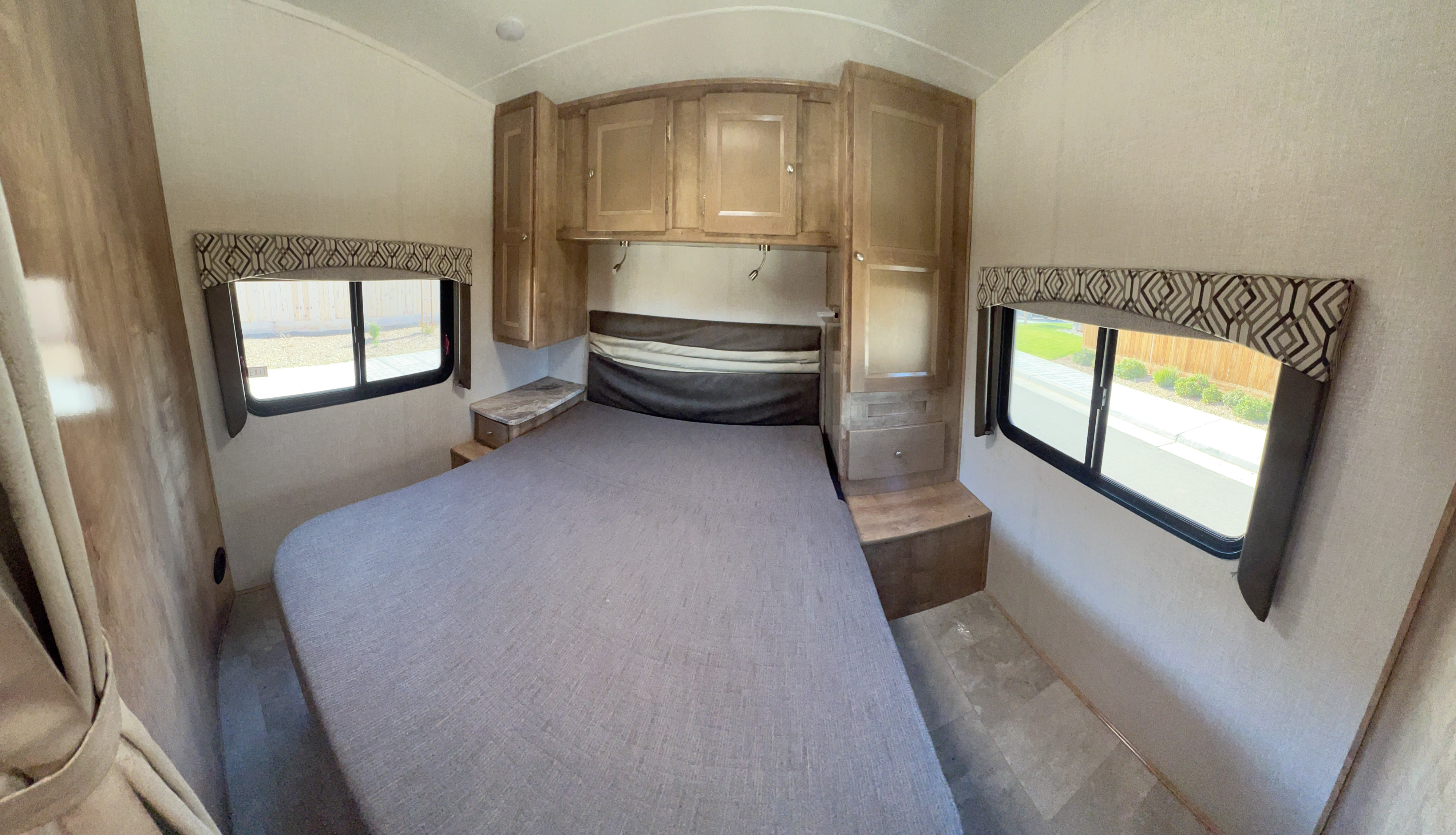 Interior of an RV rental bedroom showing a comfortable bed, overhead cabinets, and windows on both sides.. Forest River Coachmen Leprechaun 2020