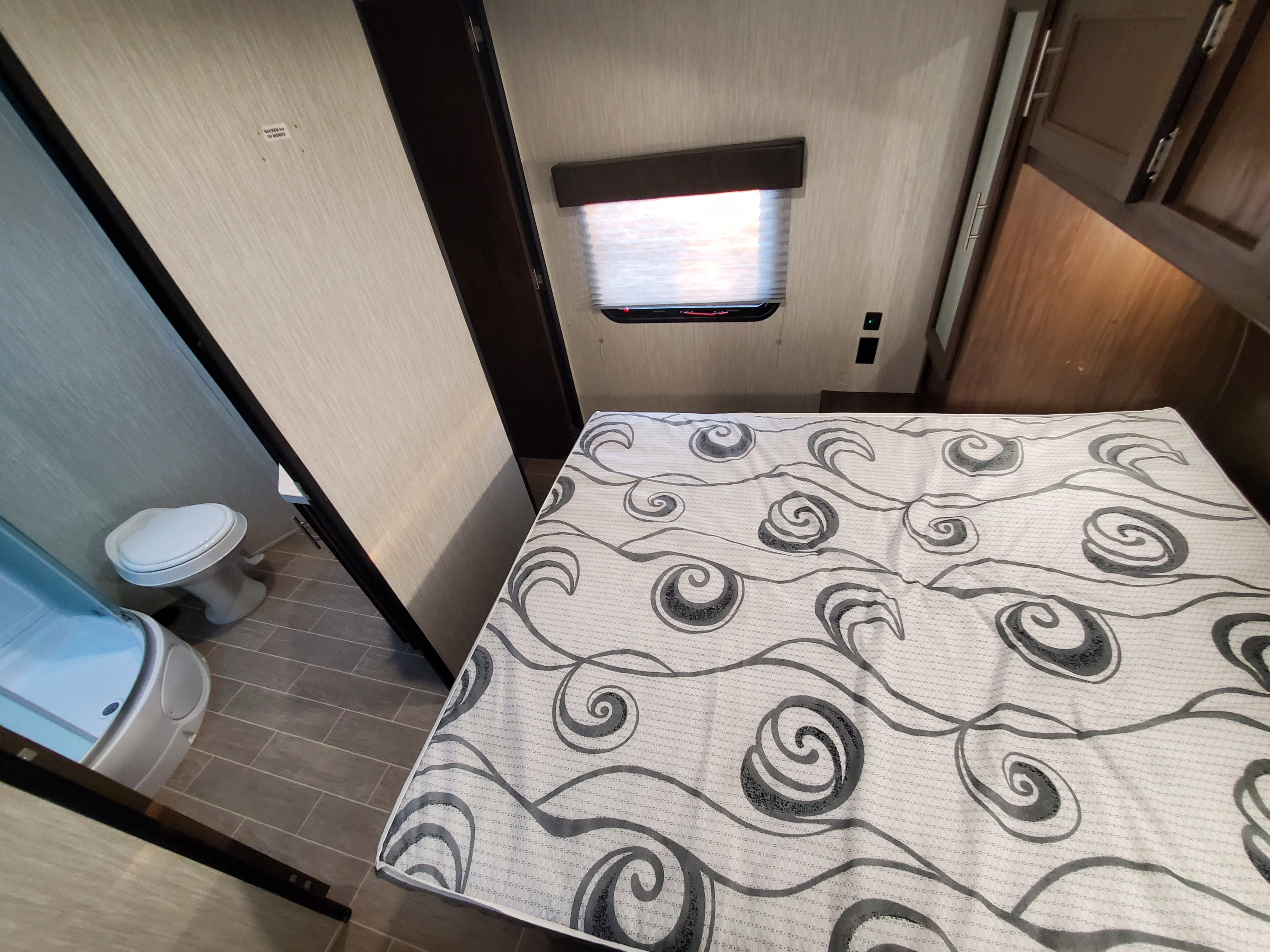 RV rental interior: bedroom with a swirly patterned bed, window, and compact bathroom featuring a toilet and shower.. Forest River patriot 2020