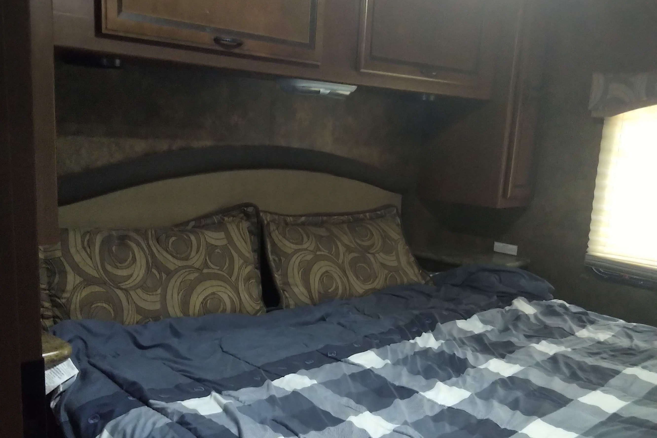 Comfortable RV rental bedroom featuring a full bed with plaid bedding, patterned pillows, and wooden overhead storage cabinets.. Thor Hurricane 2014