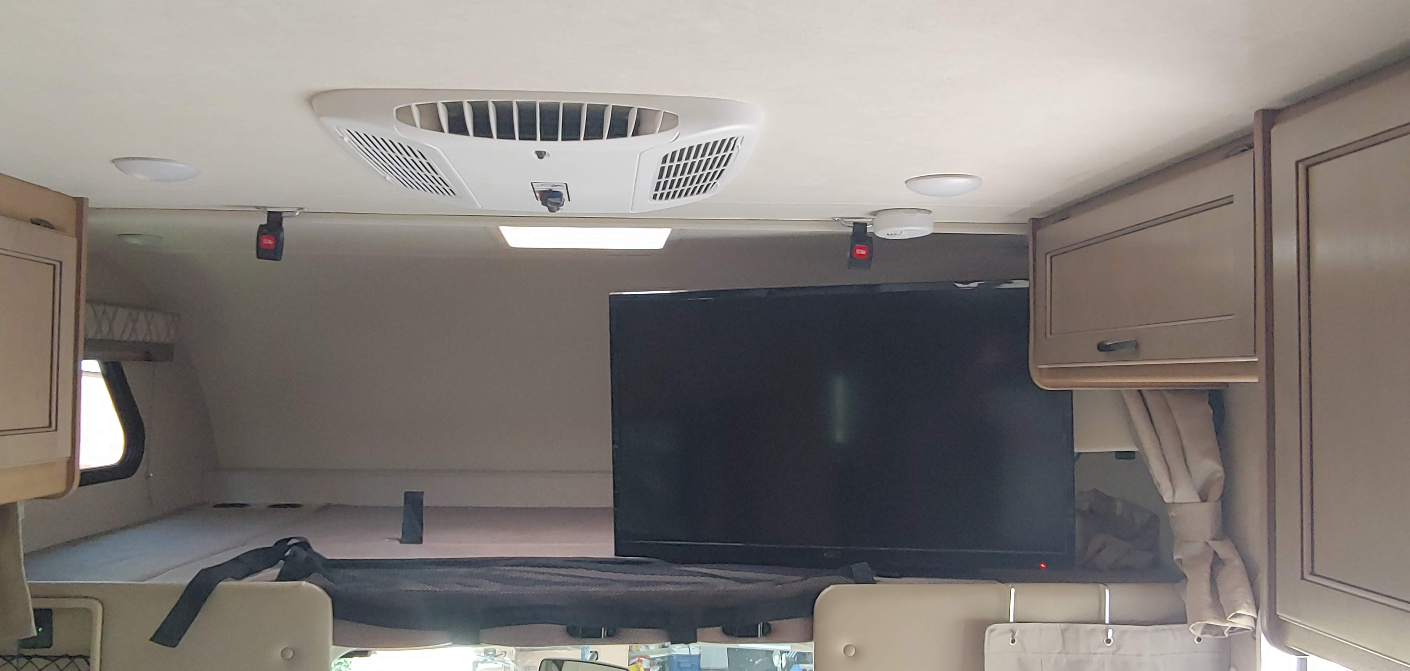 Inside an rv rental: full-size overhead bunk, wall-mounted TV, AC, and convenient storage.. Thor Four Winds 2020