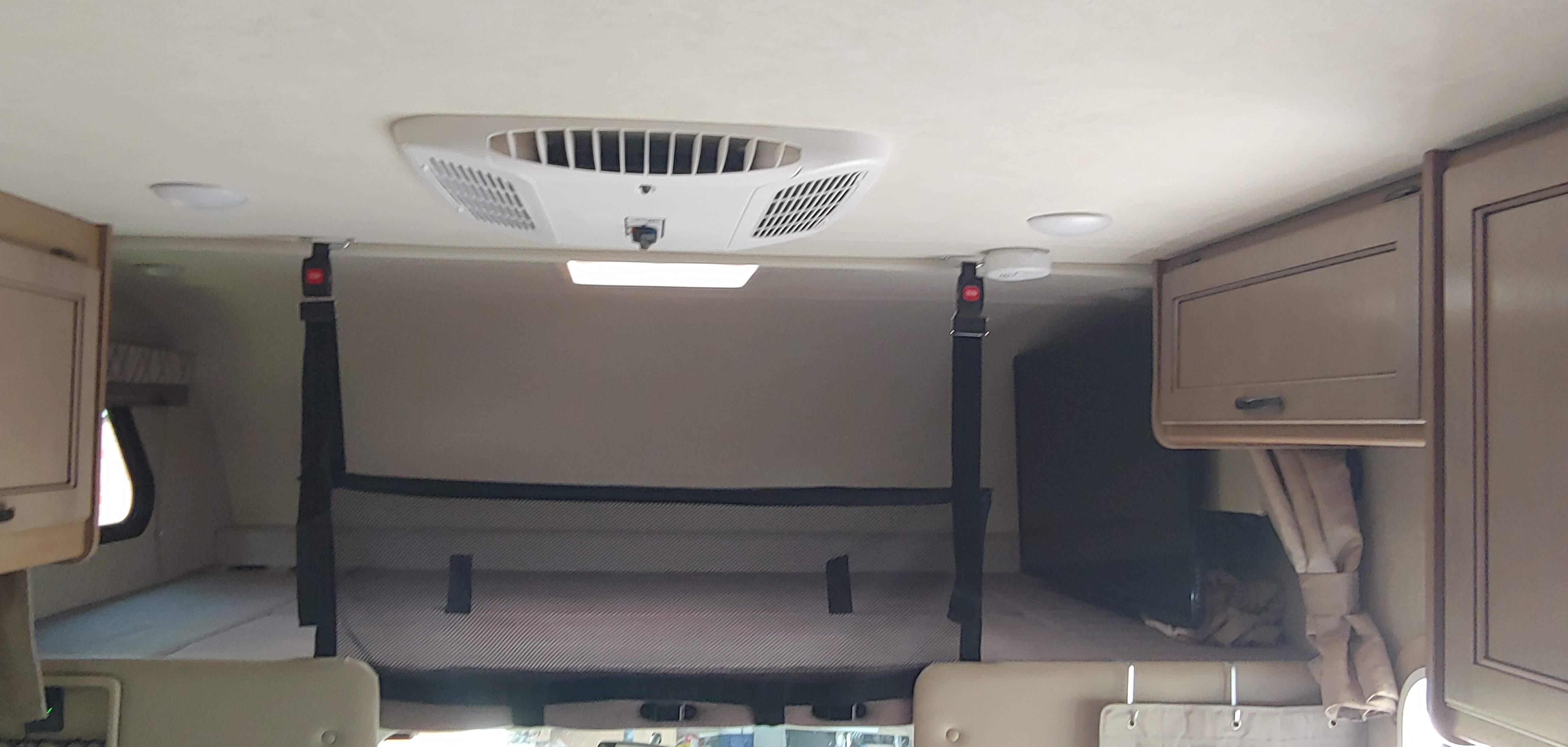 Cozy RV rental interior: overhead bunk bed with safety net, ceiling AC, smoke detector, and storage cabinets.. Thor Four Winds 2020