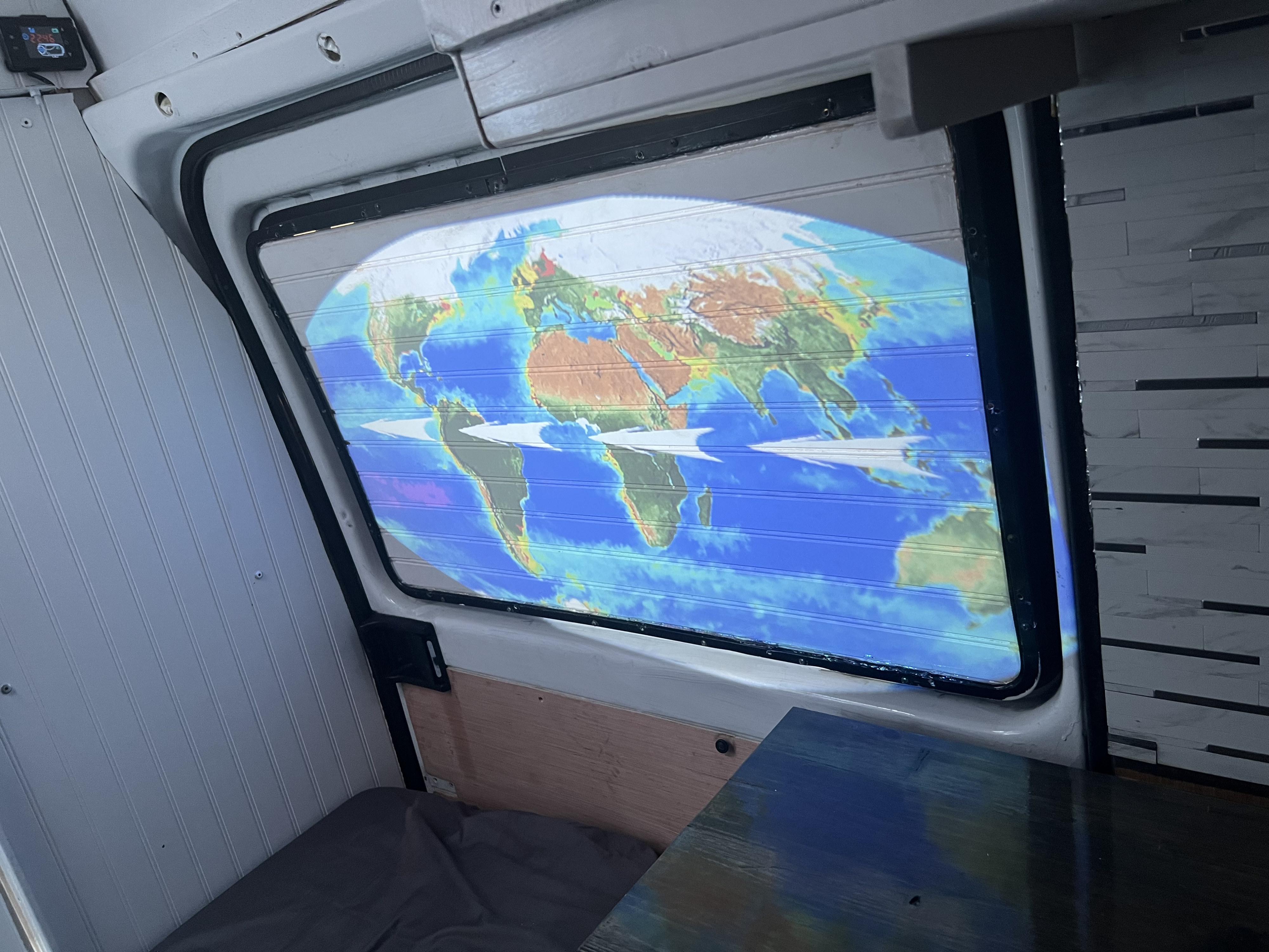Inside an RV rental, a vibrant world map is projected onto horizontal window blinds, suggesting travel dreams.. Dodge Sprinter Van 2006