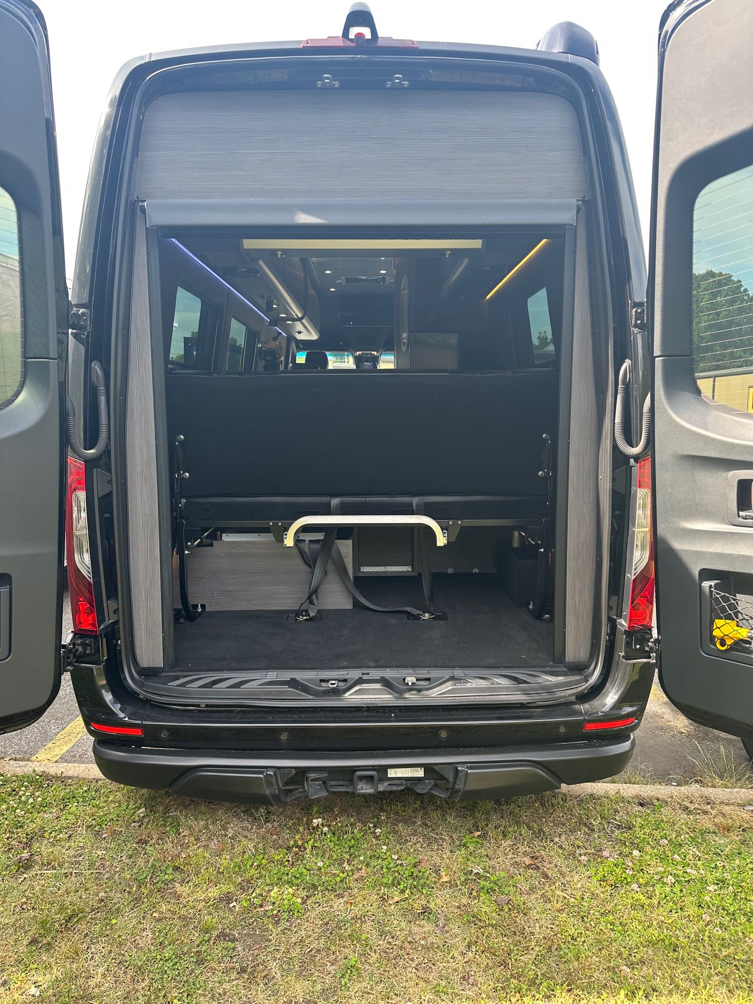 RV rental: Rear of a black camper van with open doors, showing a convertible black bench bed and storage space.. Airstream Interstate 2020