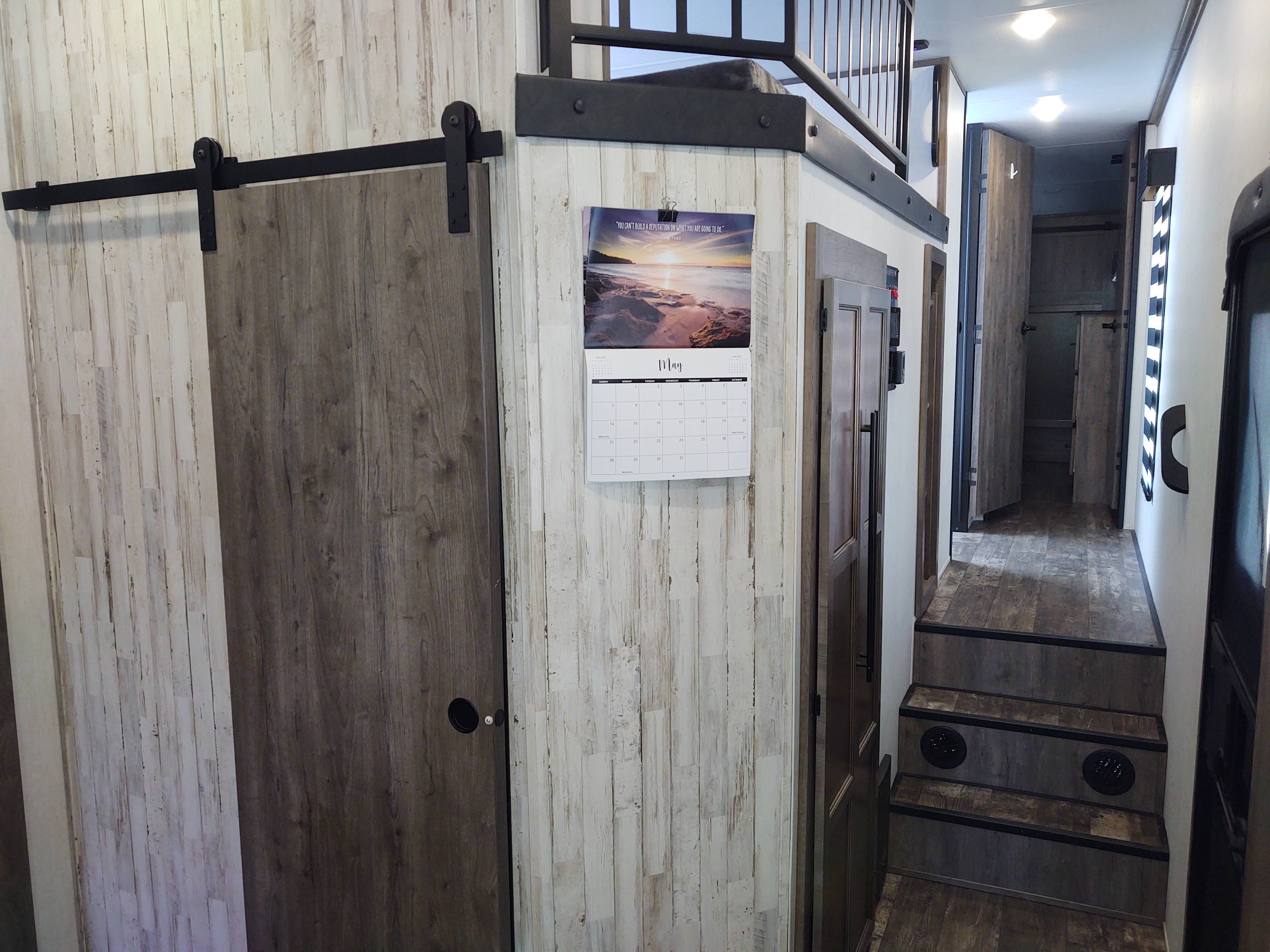 Modern RV rental interior with a sliding barn door, May calendar, and steps leading to a rear hallway. Features a compact living design.. Forest River Sabre 2021