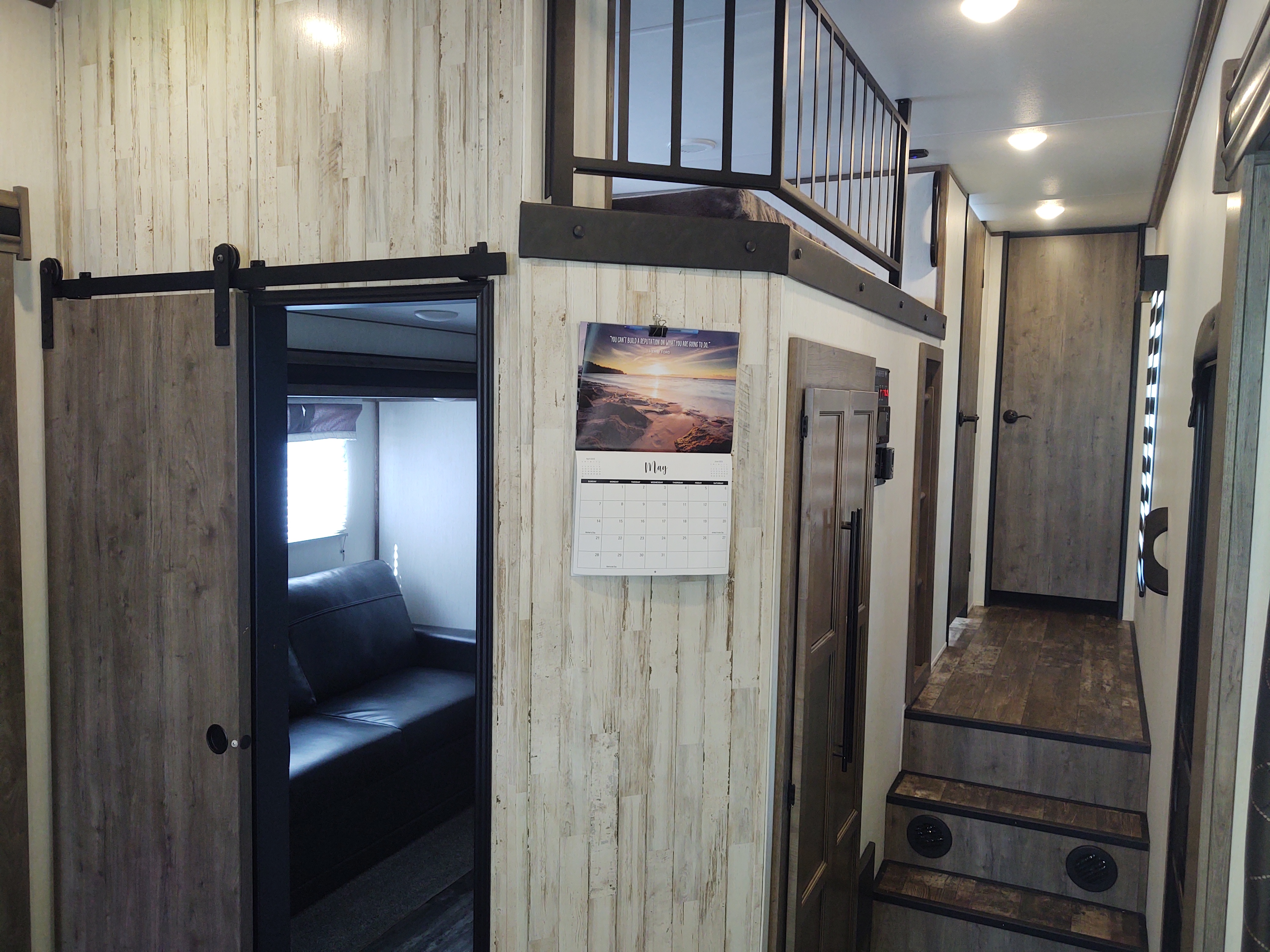Modern RV rental interior: view of a bunk-style loft with railing, steps, and a sliding barn door to a separate room.. Forest River Sabre 2021