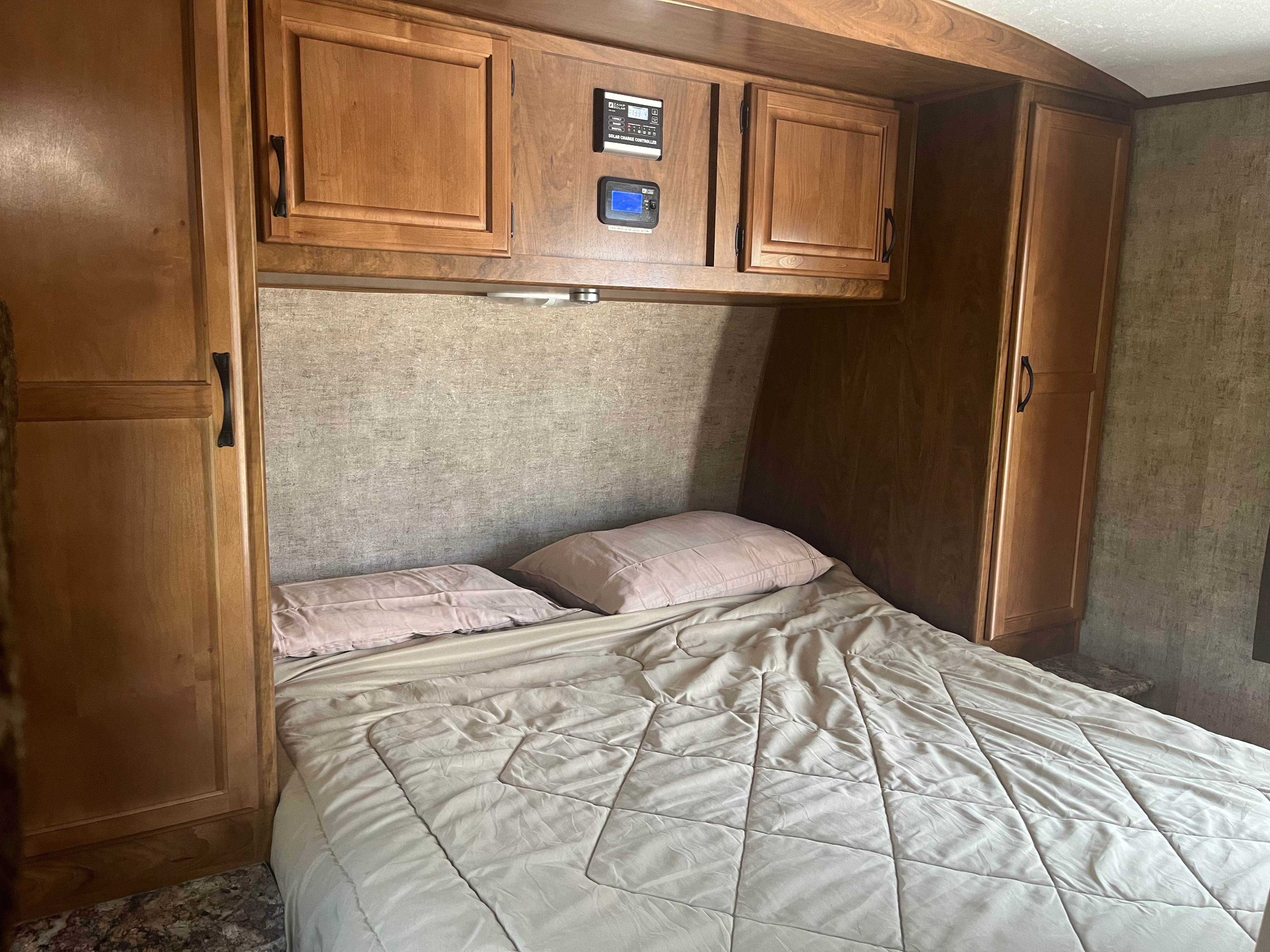 RV rental bedroom with bed, wood cabinets, and solar charge controller mounted above the sleeping area.. Outdoors RV Creekside 2017