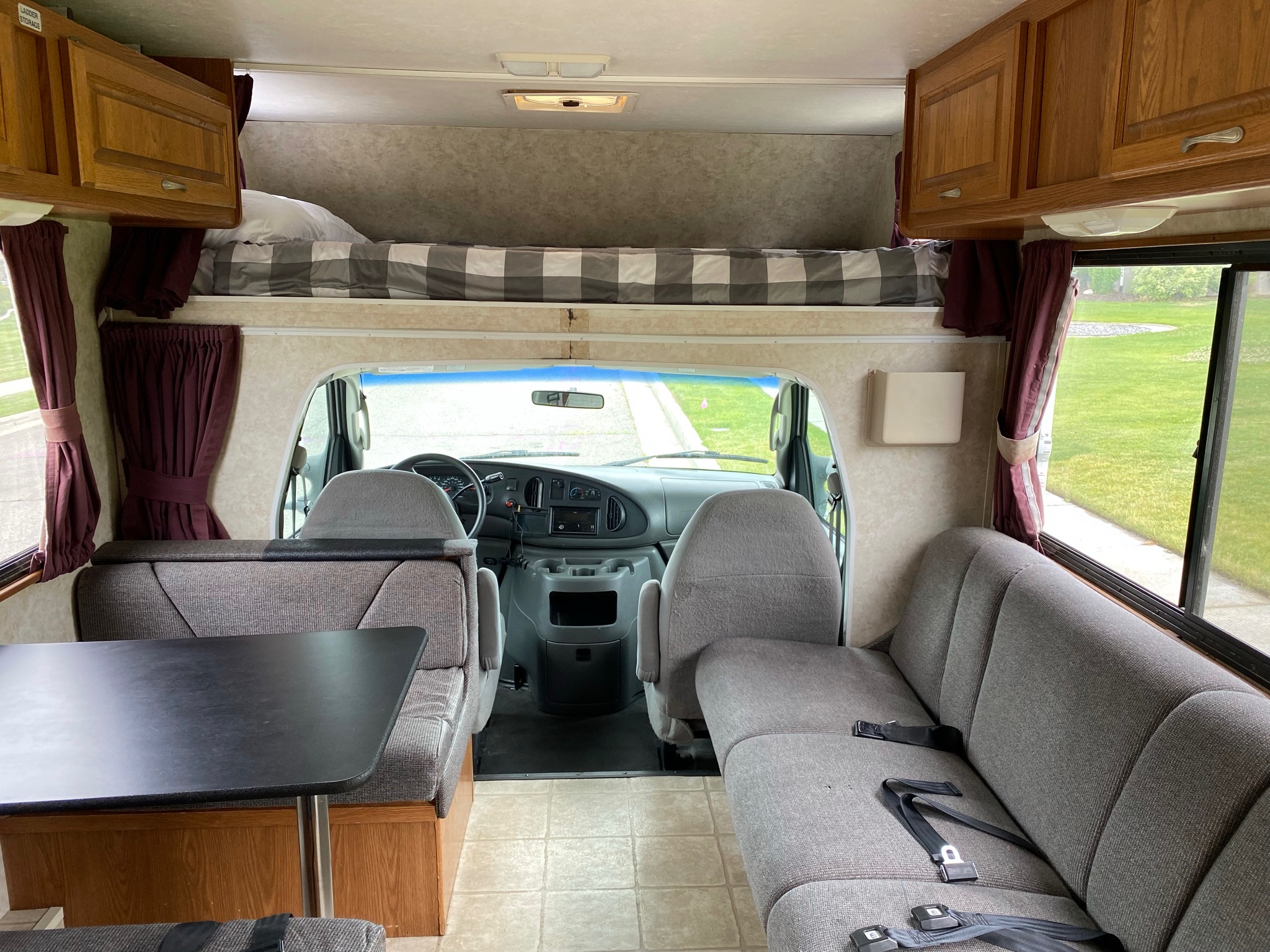 Bright rv rental interior from rear, showing cab, an overhead bunk bed, dinette, and long sofa seating.. Four Winds Majestic 2004
