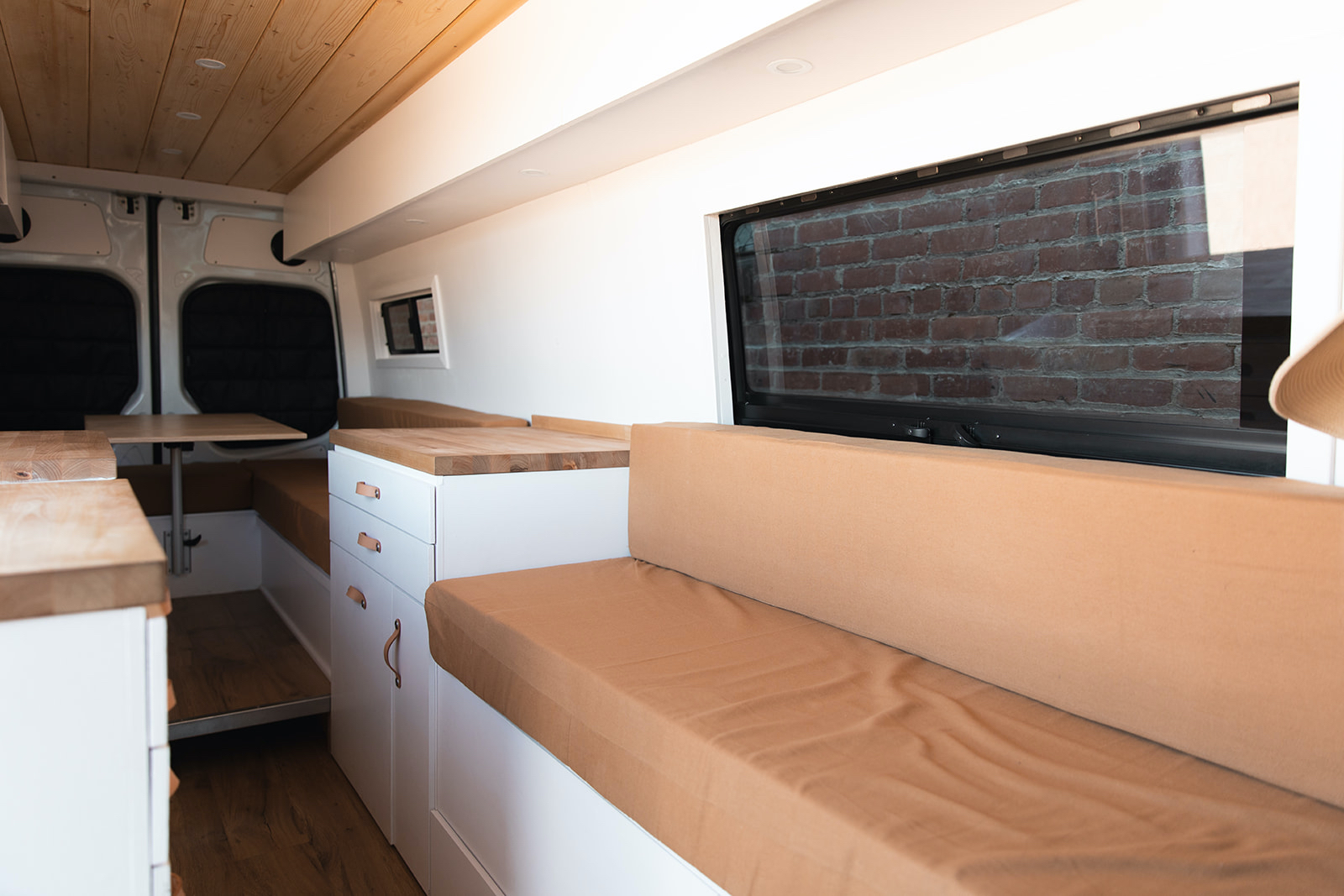 Bright RV rental interior: Custom camper van with clean white cabinets, wooden tops, and cozy tan cushions.. Mercedes-Benz Sprinter 2014