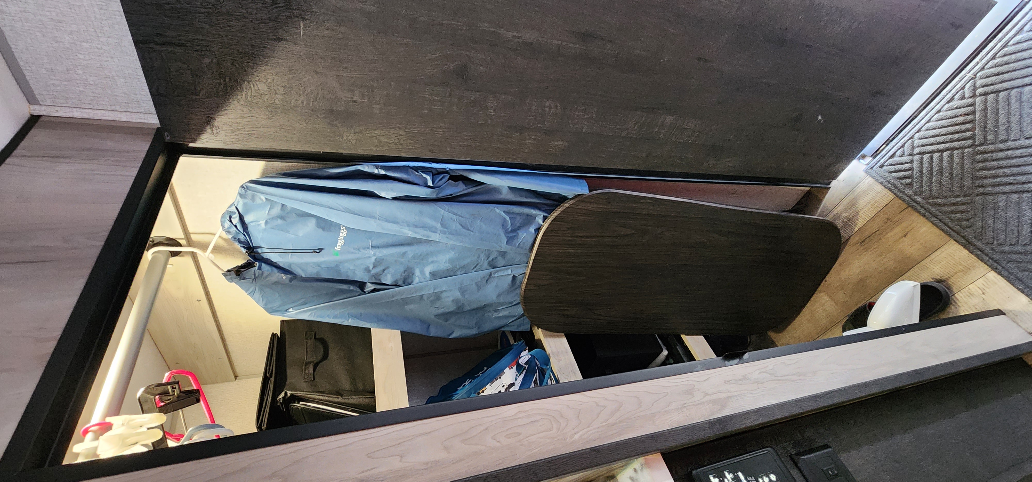 RV rental storage compartment: A blue rain jacket, portable dark wood table, and hangers are neatly placed inside.. KZ Connect 2022