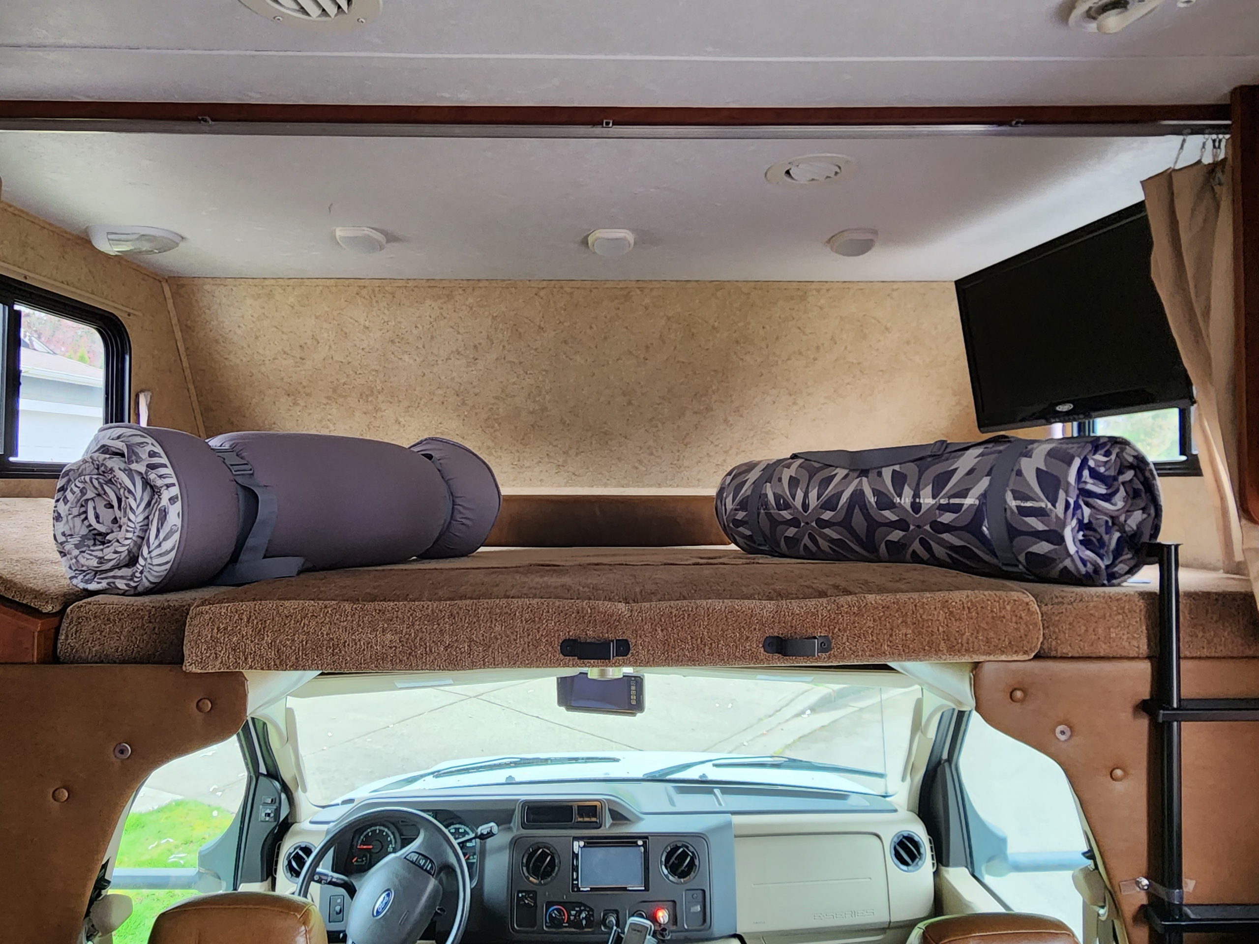 Spacious rv rental interior featuring a cozy overhead bunk with sleeping pads and a view of the motorhome's cockpit.. Forest River Sunseeker 2013