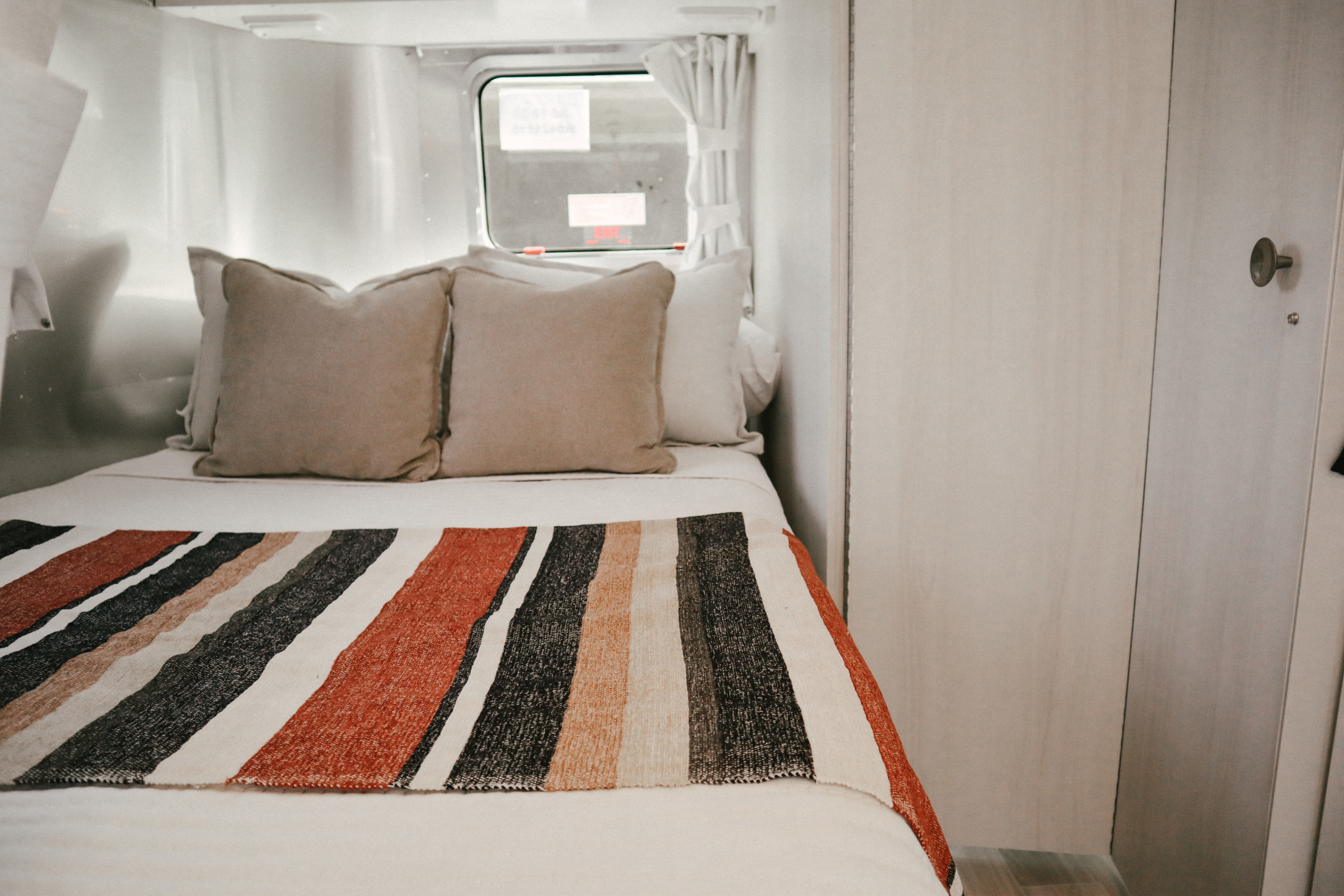 Cozy bed inside a clean, modern RV rental, with a colorful striped blanket and pillows. Ideal for comfortable travel.. Airstream Bambi 2023