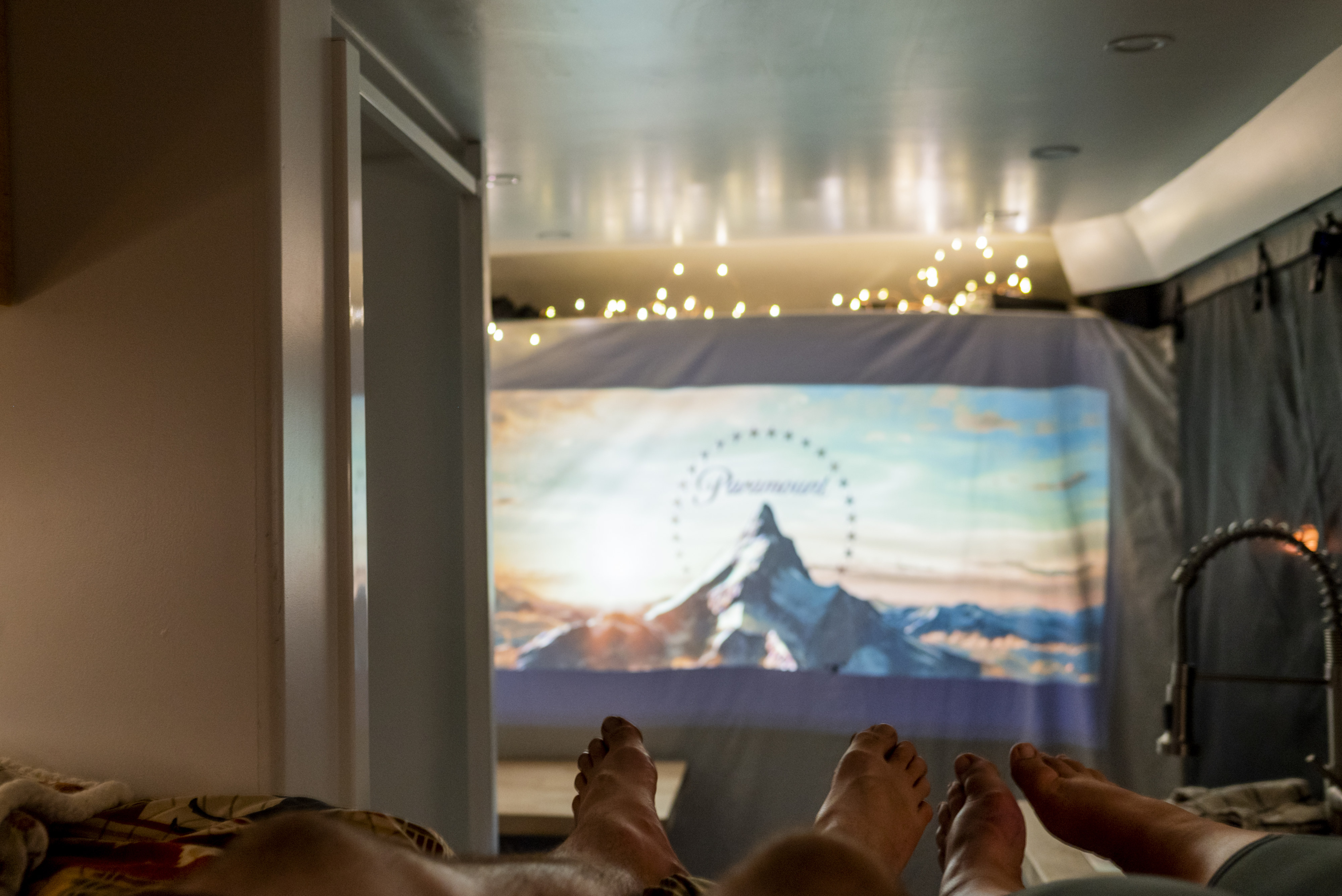 Cozy RV rental experience: feet up, enjoying a movie with the iconic Paramount logo projected inside.. Dodge Ram Promaster 3500 2021